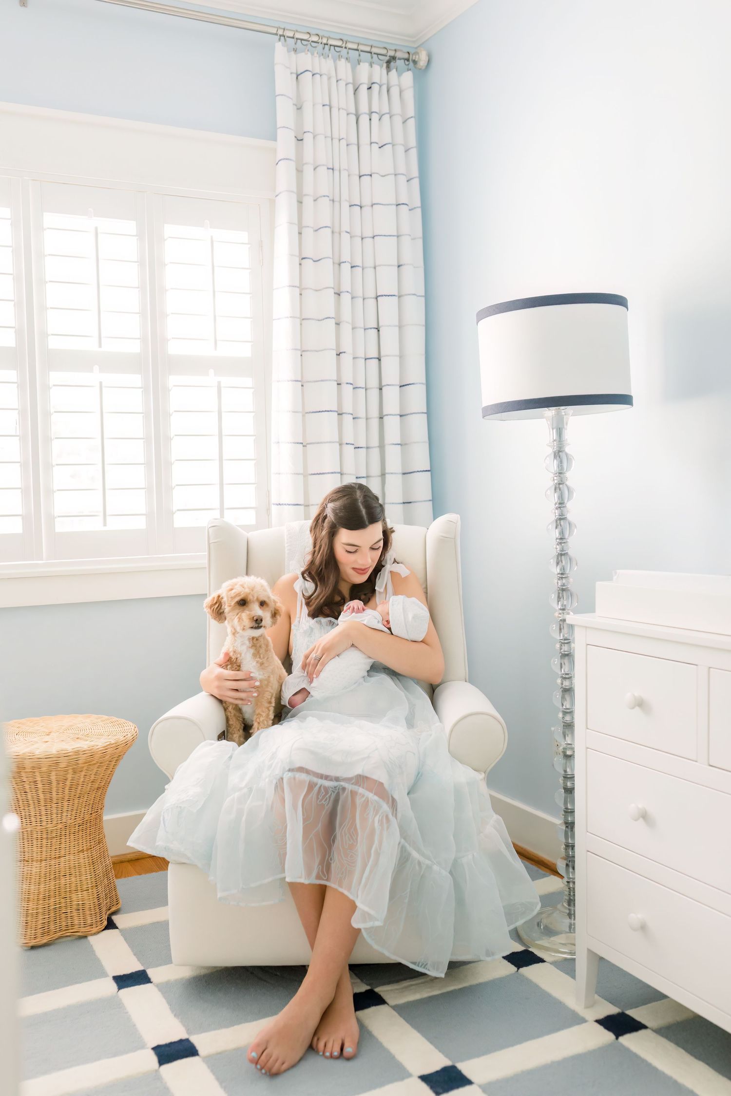 Woman sitting in nursery chair with golden retriever and baby.
