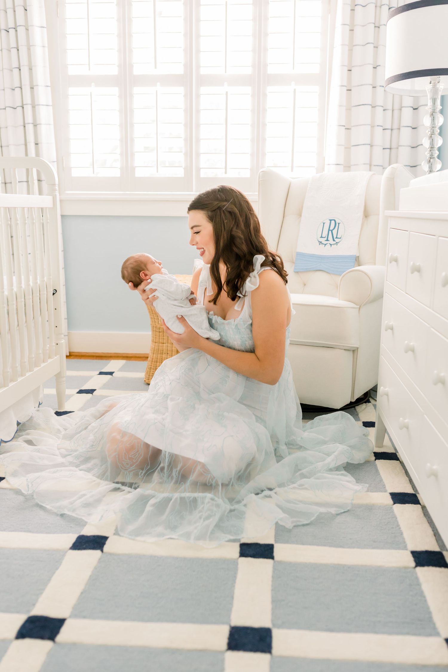 Woman in flowing dress sitting on nursery floor with baby.