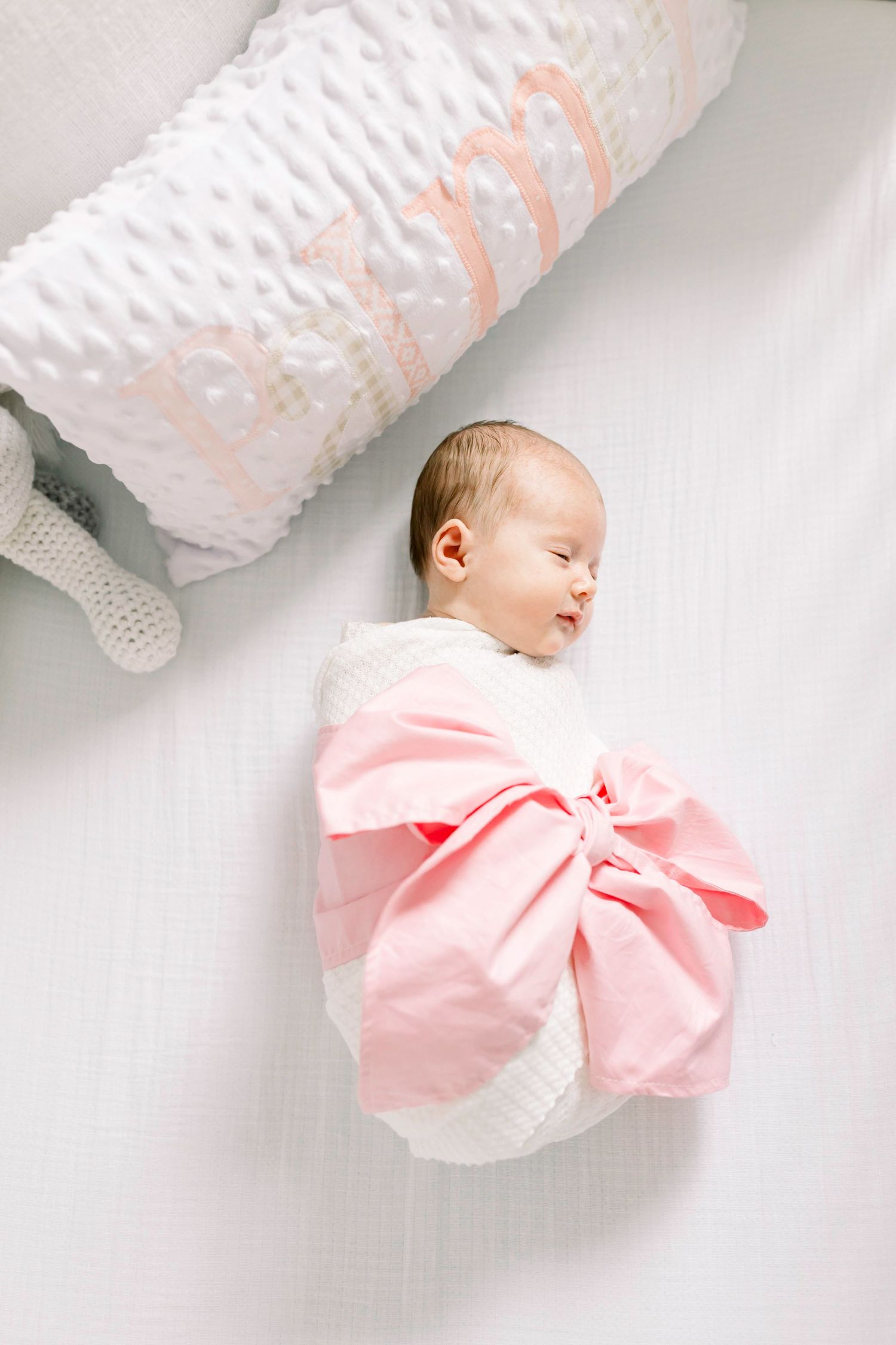 Sleeping newborn baby wrapped in pink bow swaddle against white background.