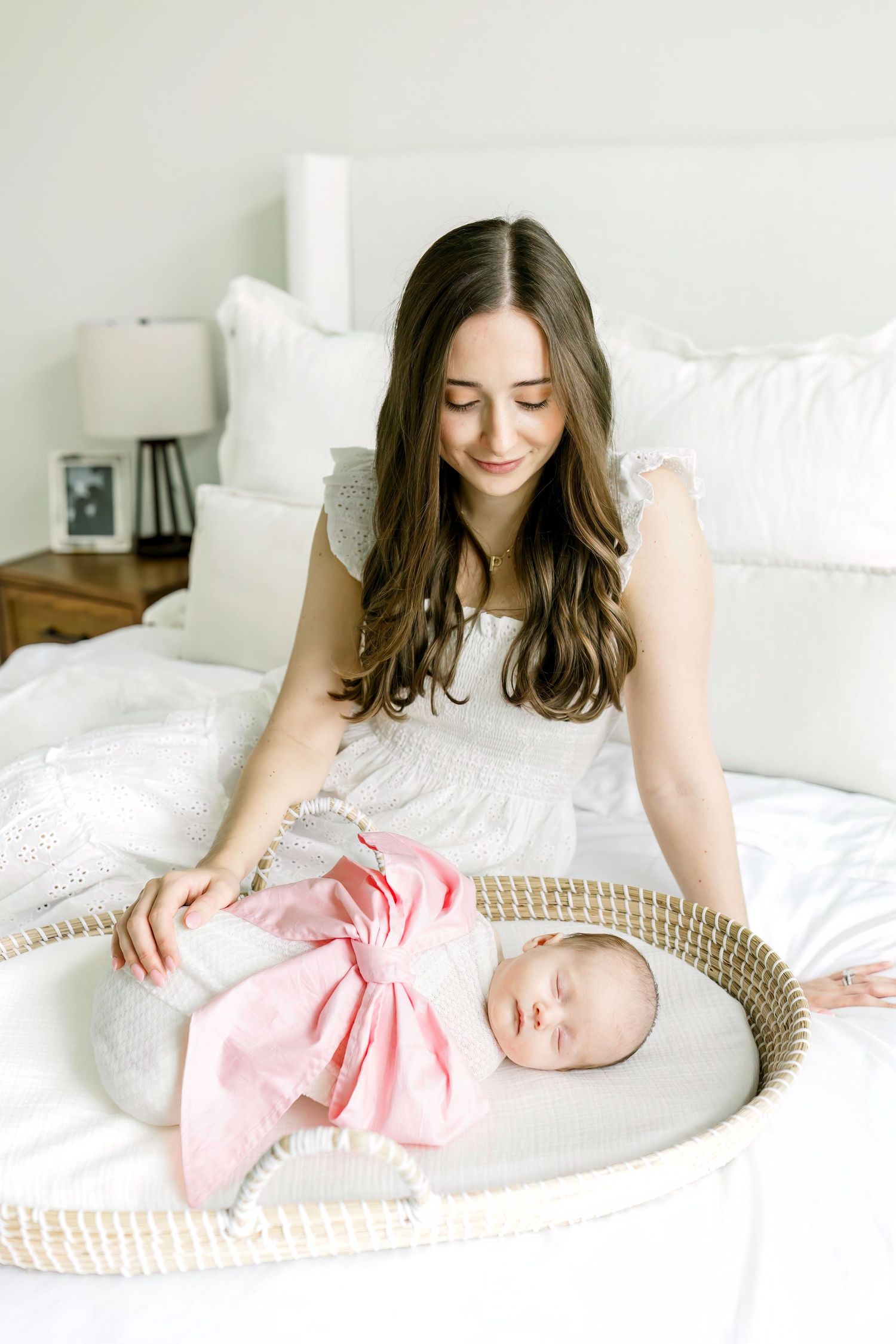 Mother watching over sleeping newborn in woven basket on white bedding.