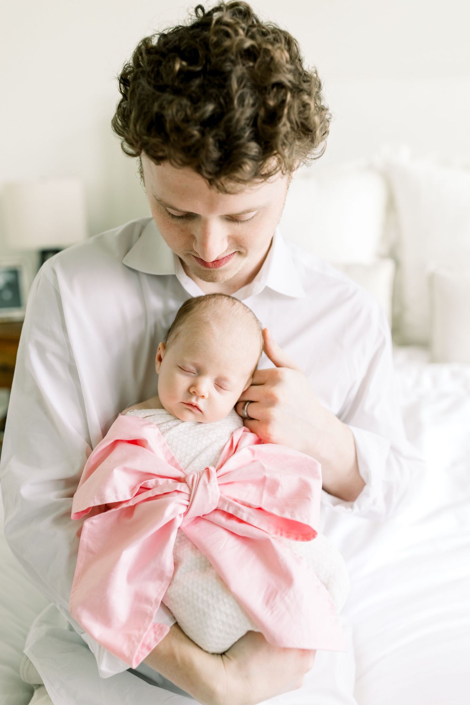 Parent in white shirt holding sleeping newborn wearing pink bow wrap.