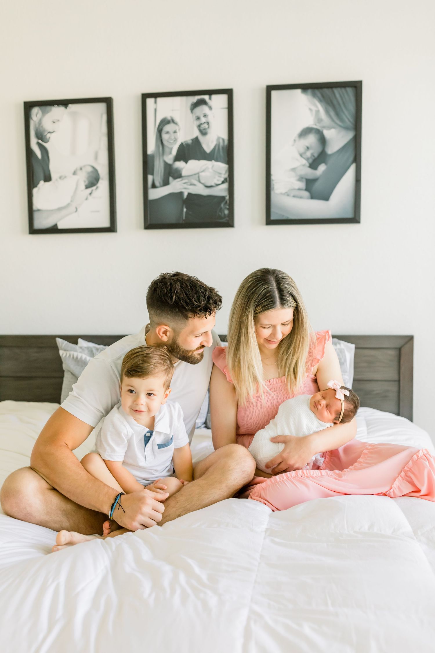 Family sitting on bed with children and framed photos on wall.
