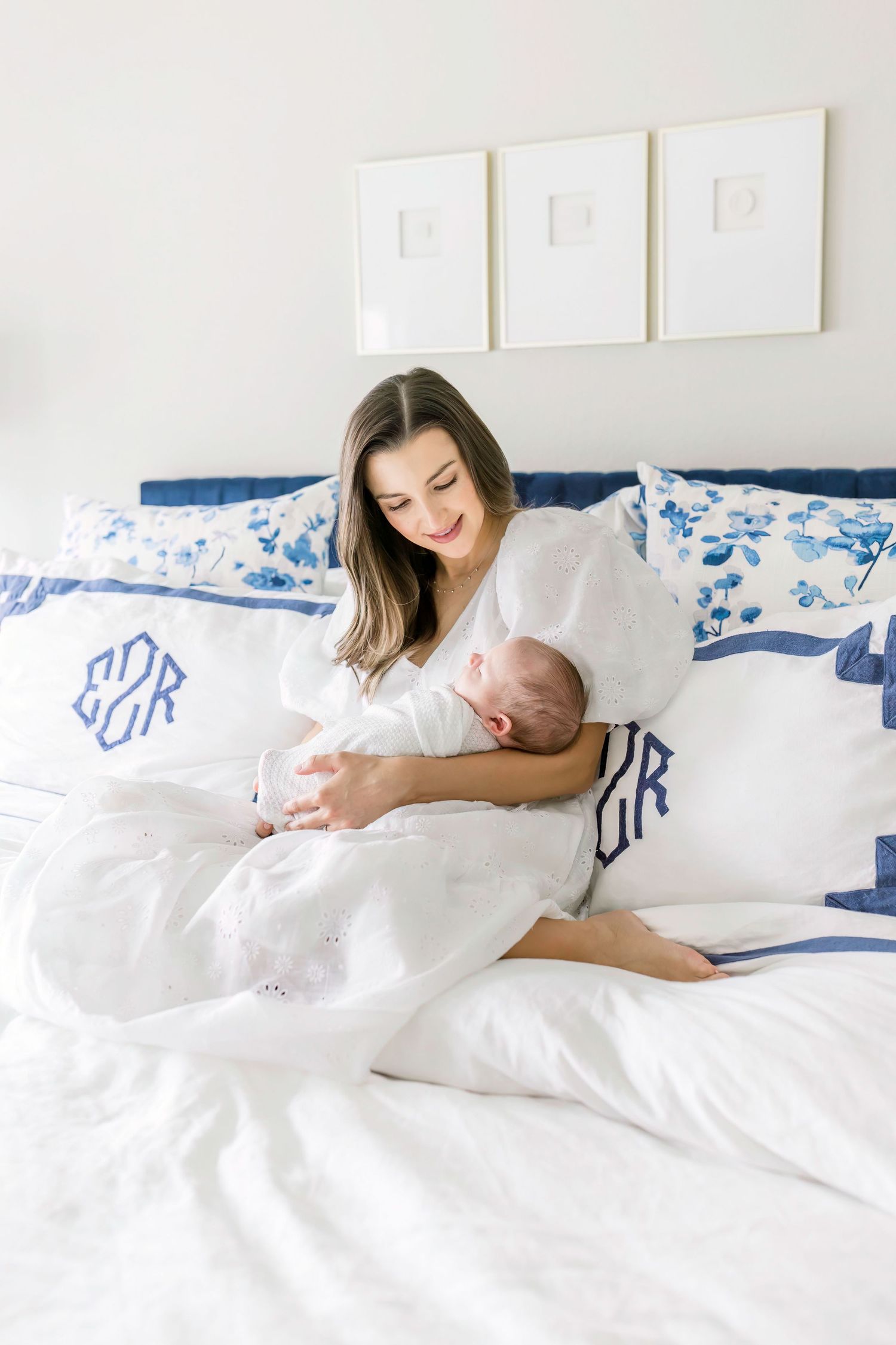A tender moment between parent and baby on a bed with blue and white monogrammed pillows.