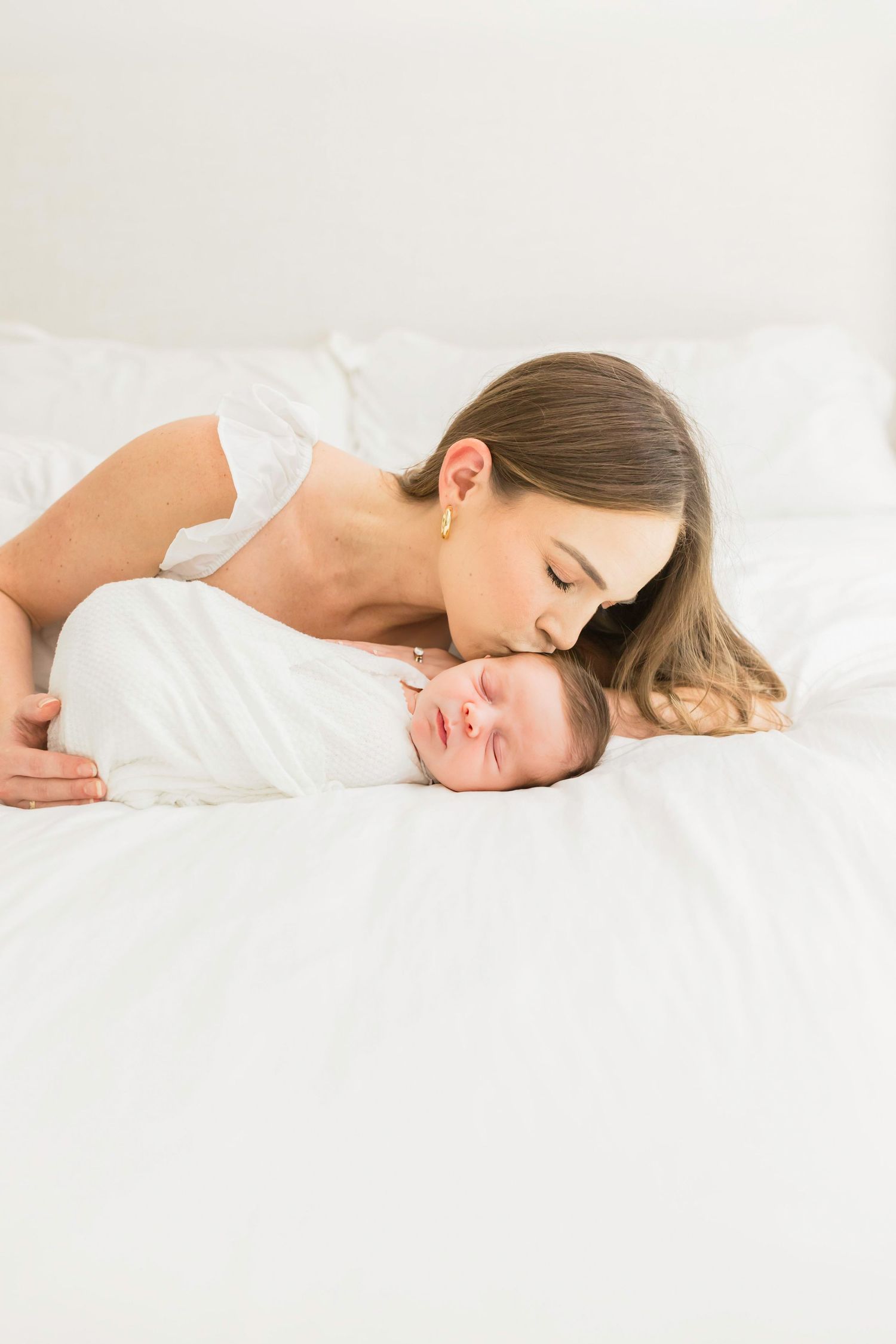 Intimate moment between parent and newborn baby on white bedding.