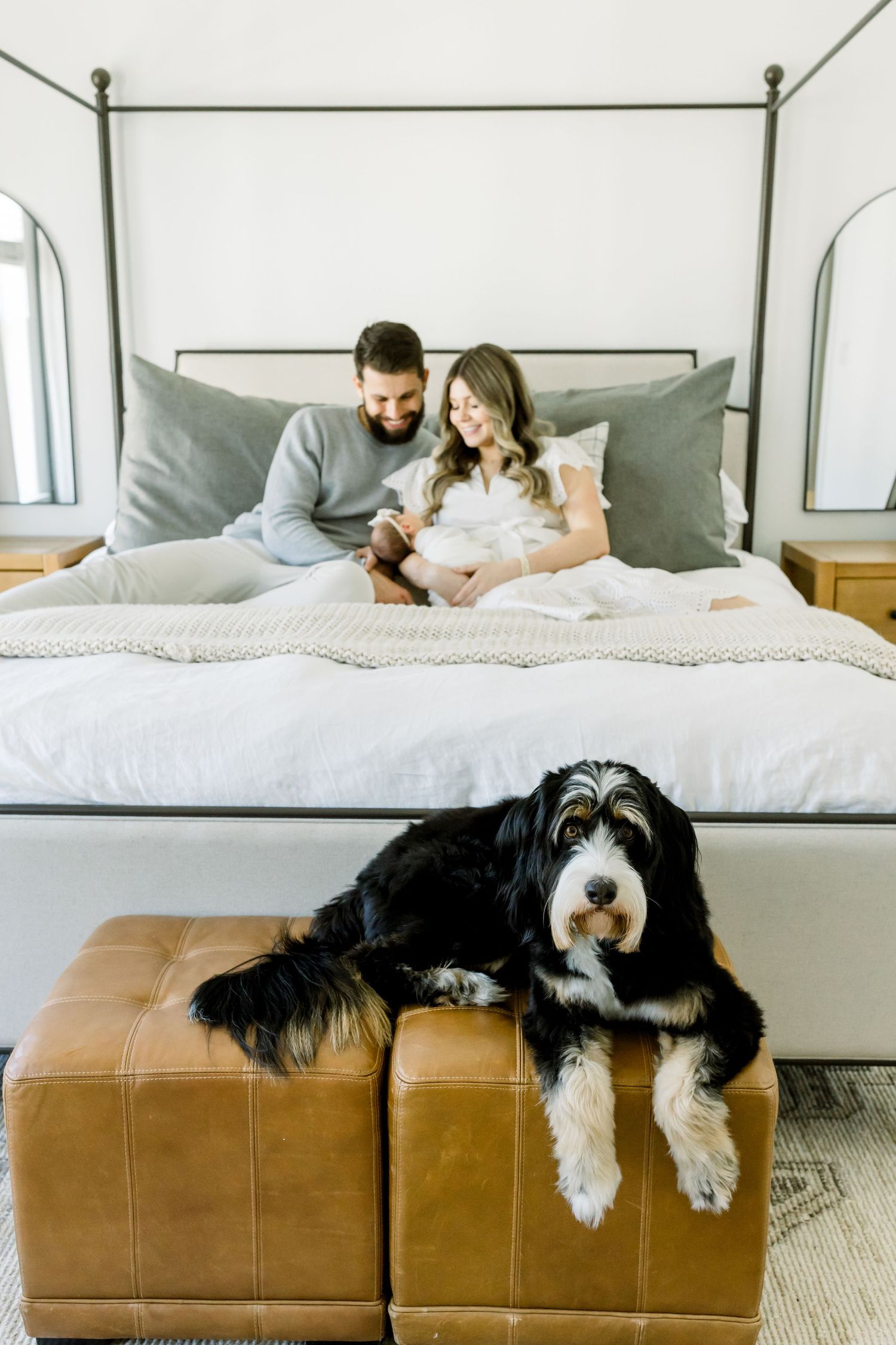 Modern bedroom scene with family and black and white dog on leather ottoman.