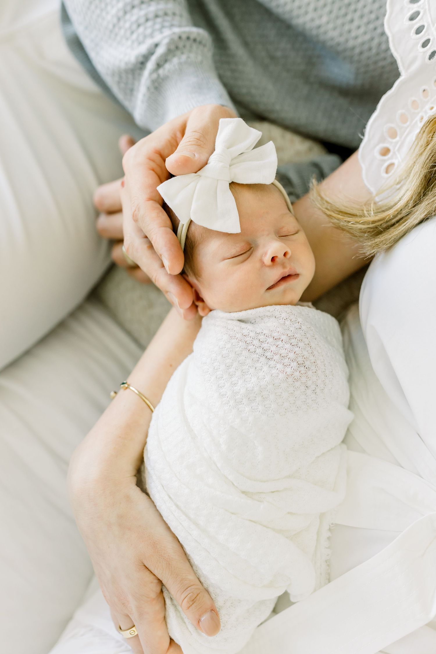 Peaceful sleeping baby with white bow headband wrapped in soft white blanket.