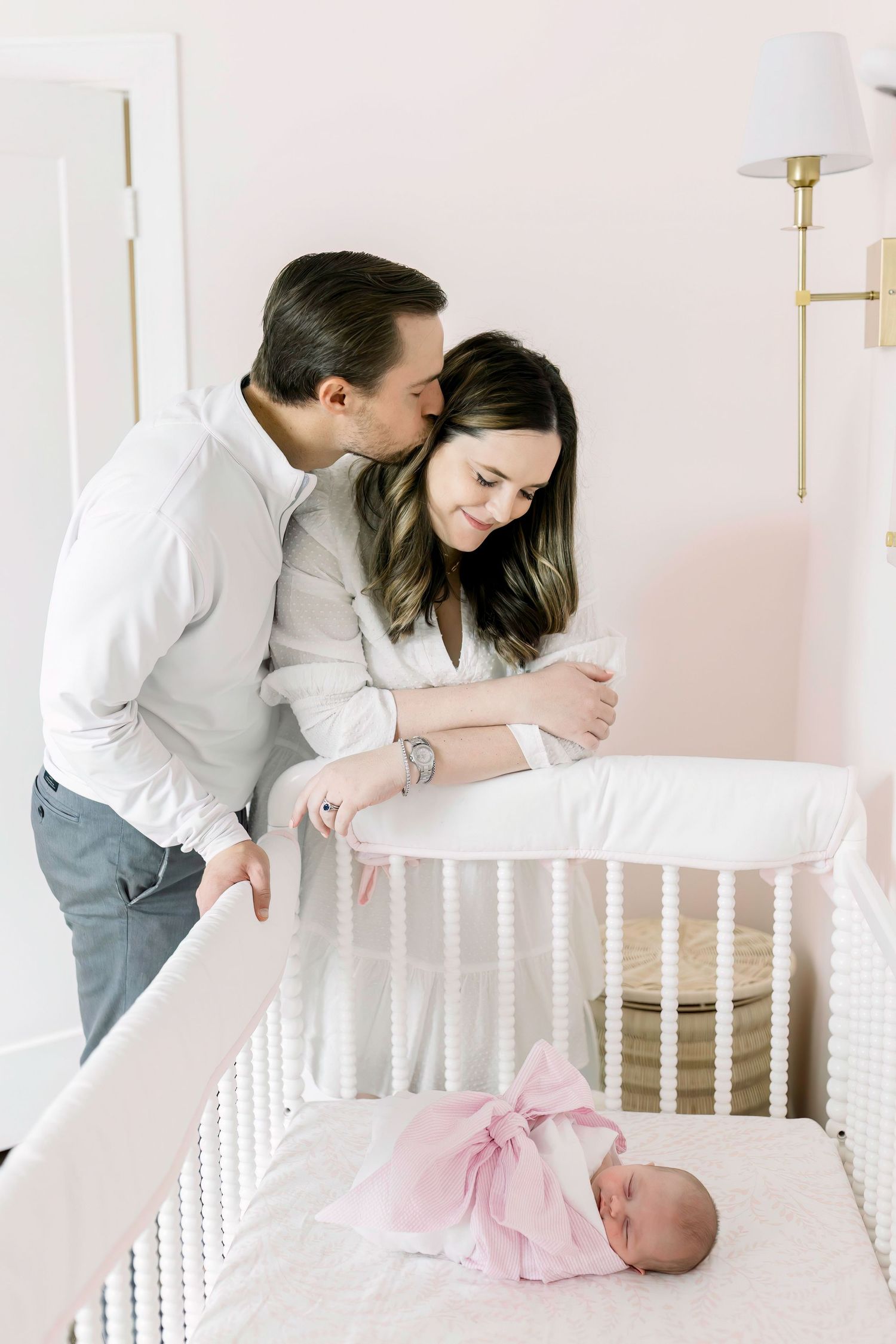 A tender moment between parents looking down at their sleeping baby in a white crib.