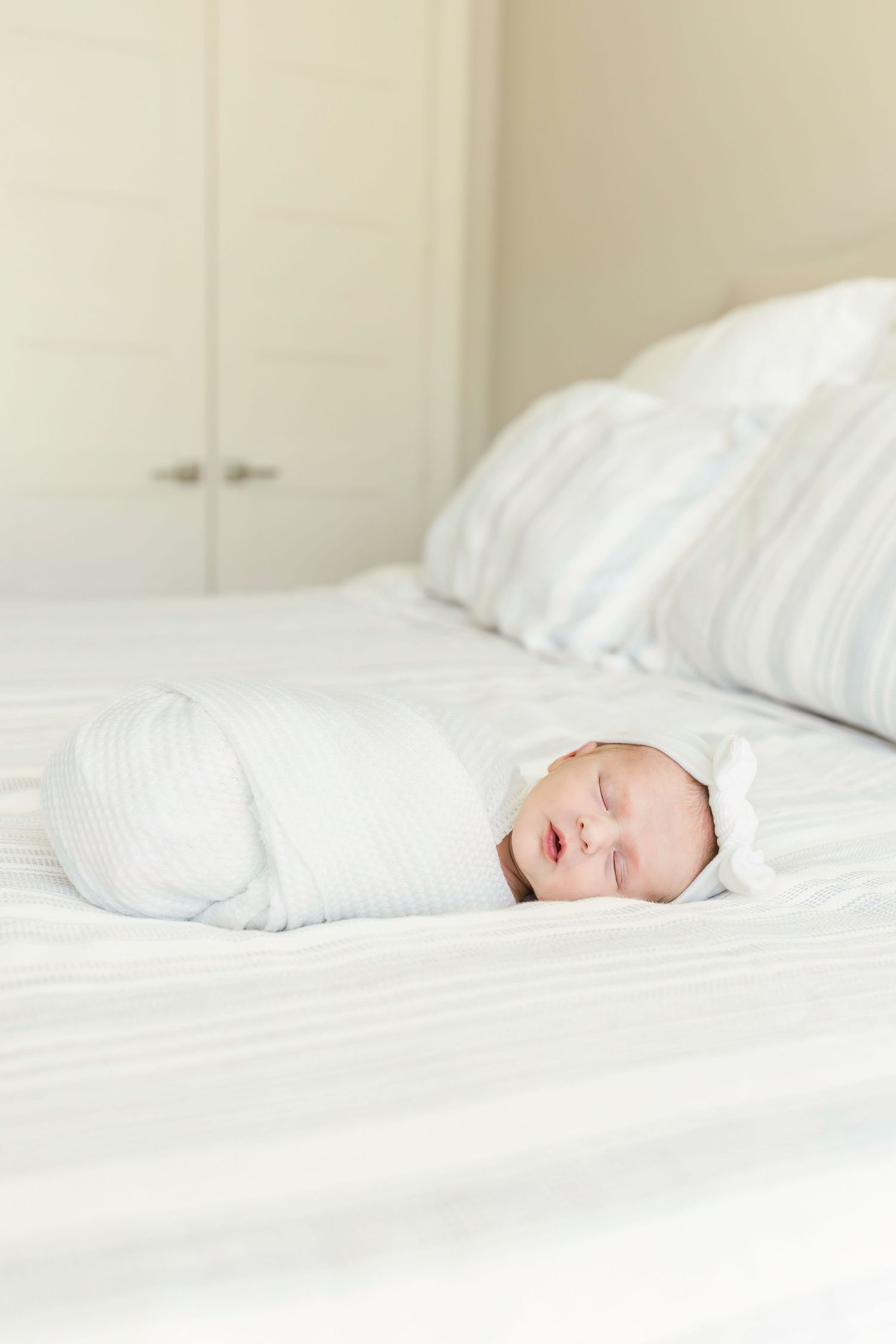 Sleeping newborn wrapped in white swaddle on crisp white bedding.