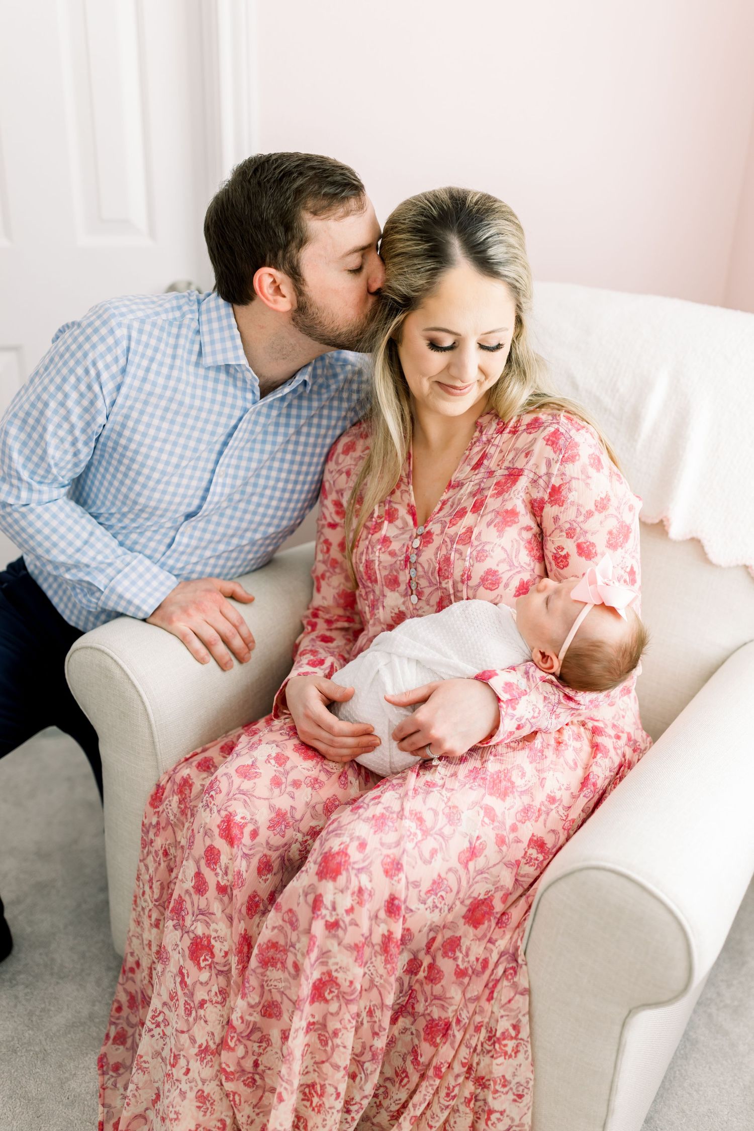 A couple sits on a white couch sharing an intimate moment with their newborn baby.