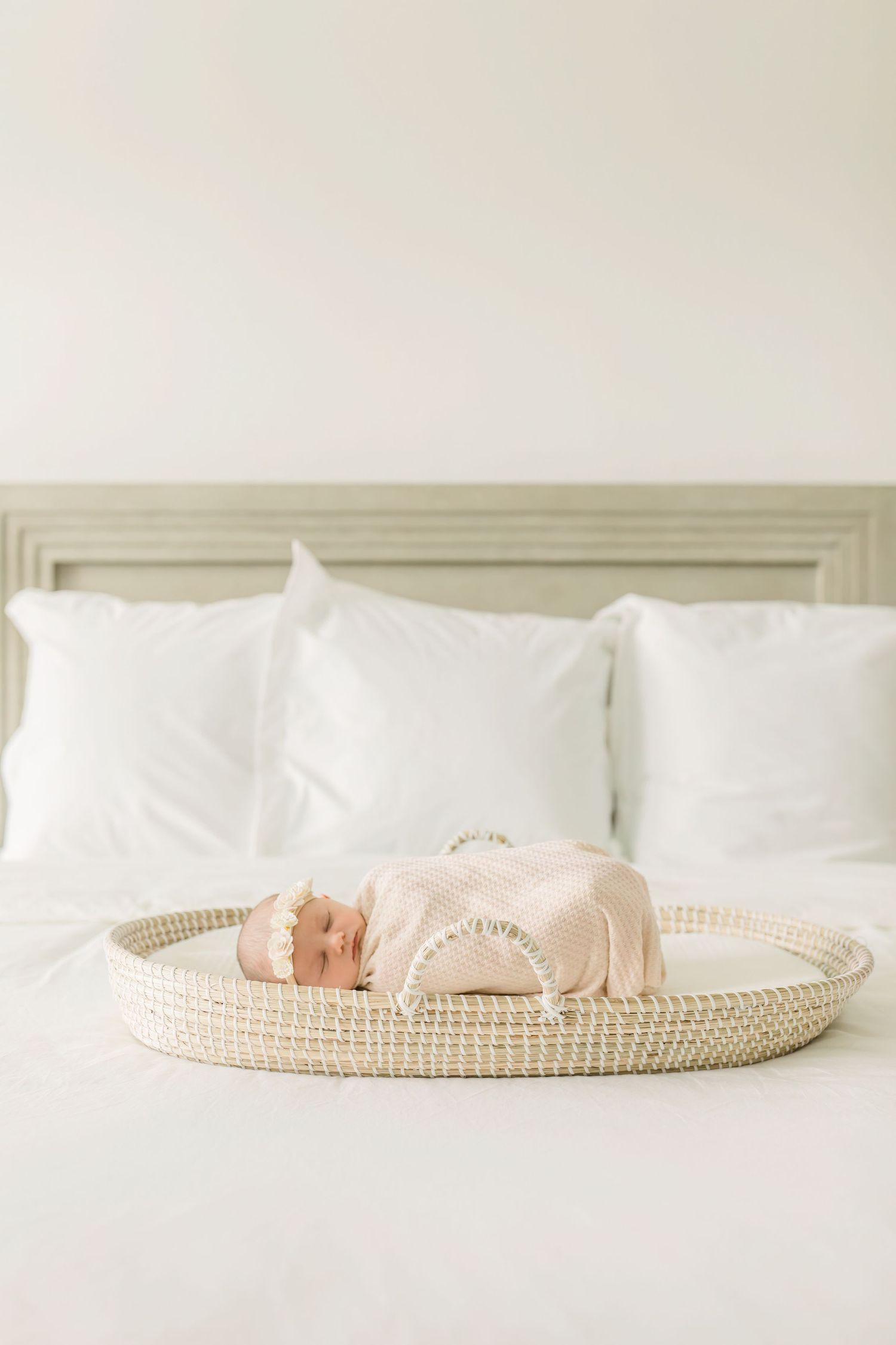 Newborn baby sleeping peacefully on a woven basket tray on white bedding.
