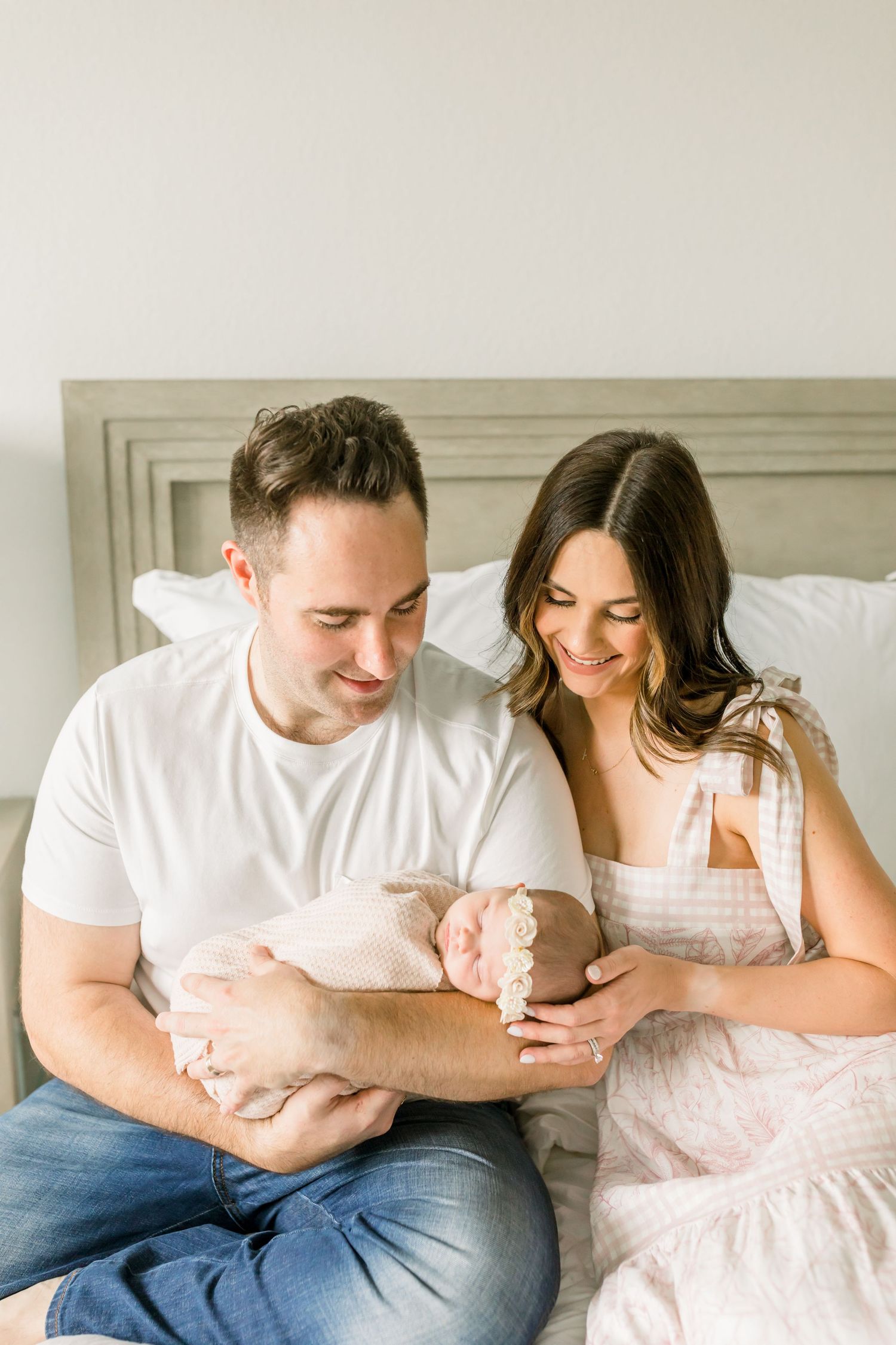 Family scene of parents with newborn baby on white bed.