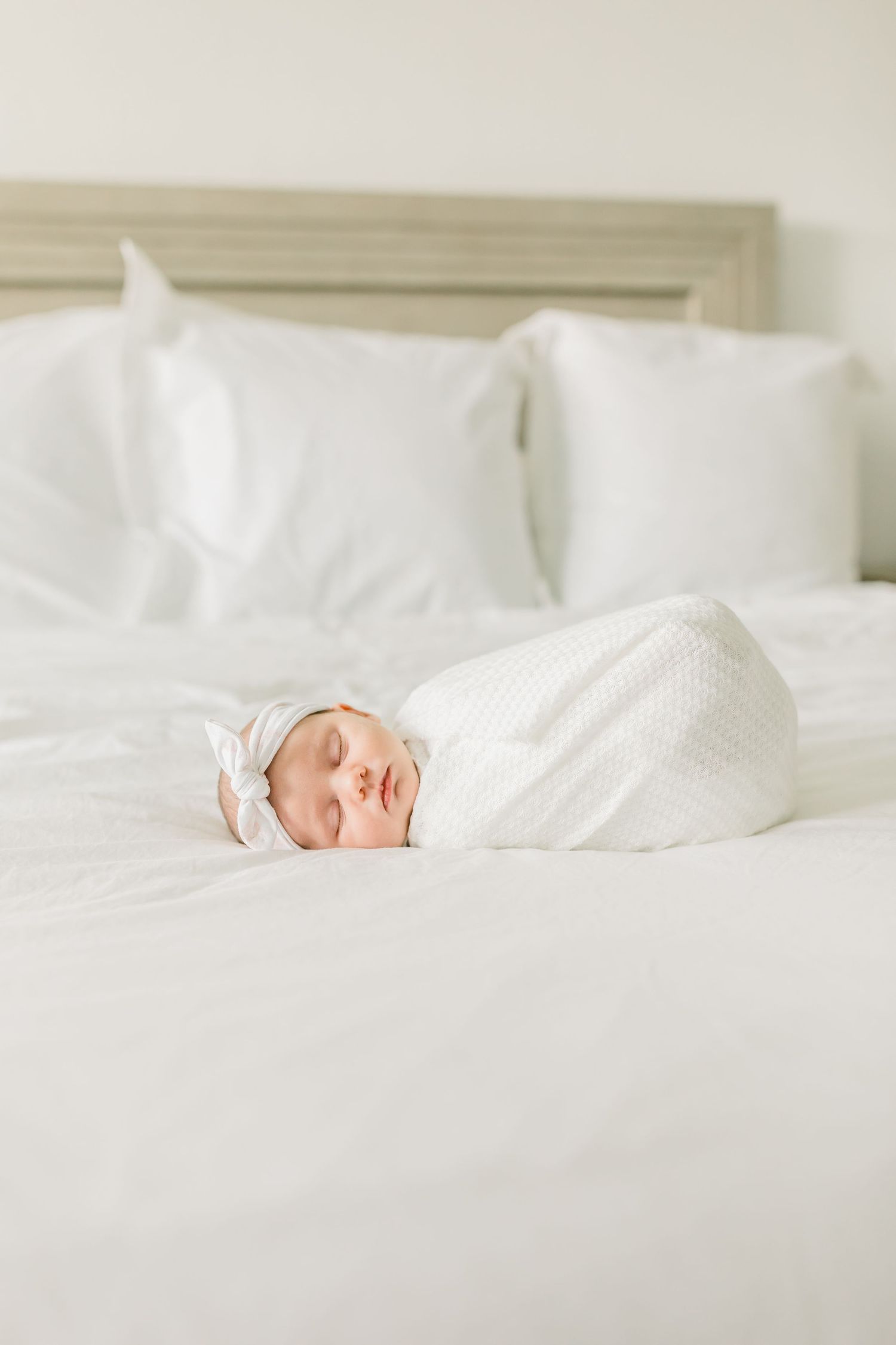 Sleeping newborn wrapped in white swaddle on white bedding.