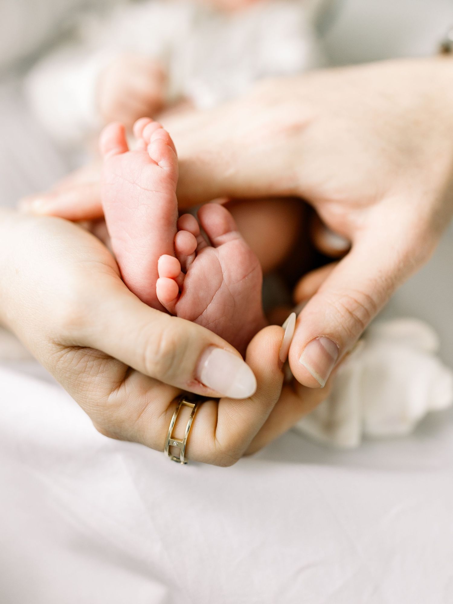 Gentle hands cradle tiny newborn feet against soft white fabric.