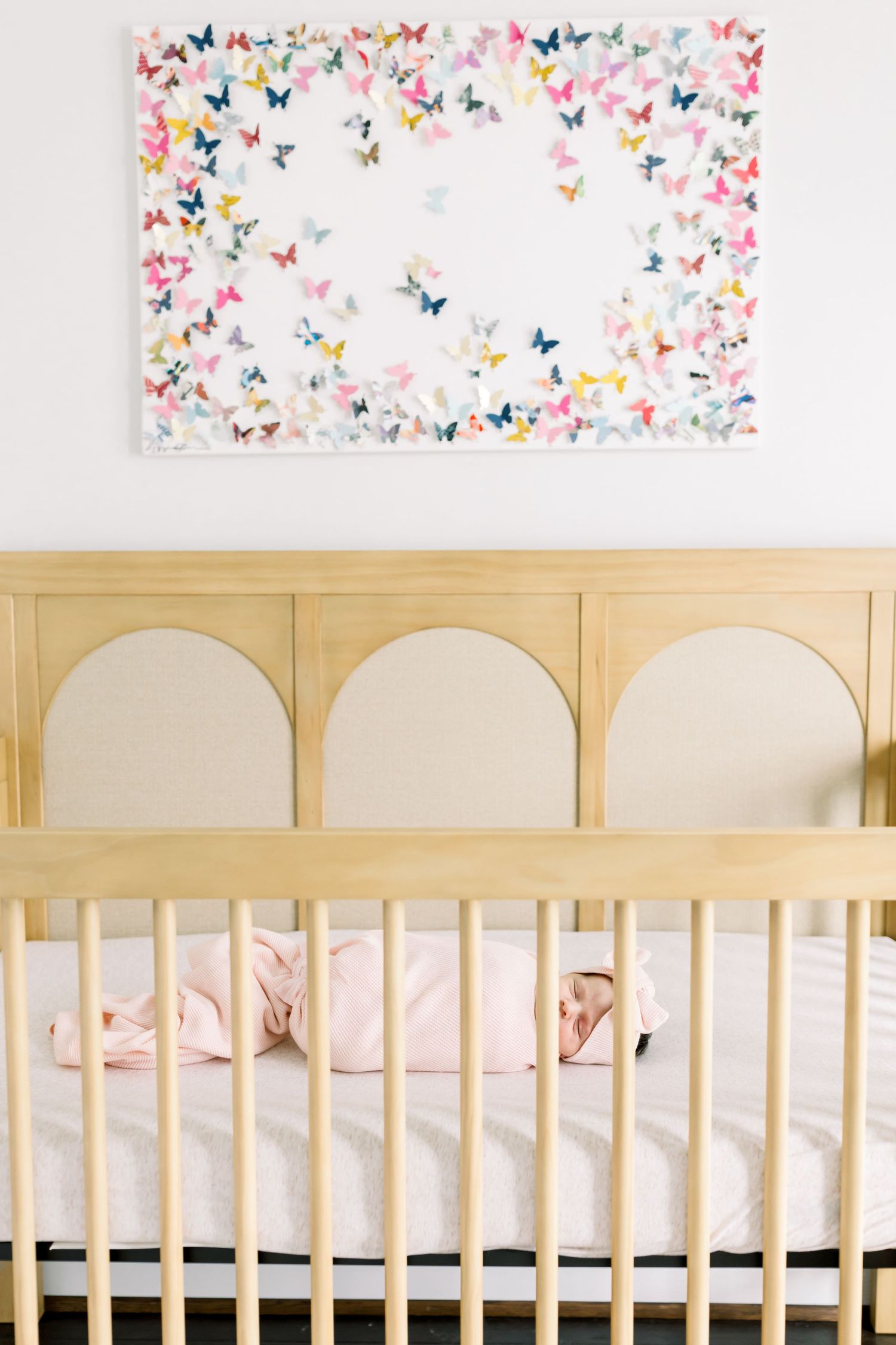 Natural wood crib with butterfly artwork above and pink bedding inside.