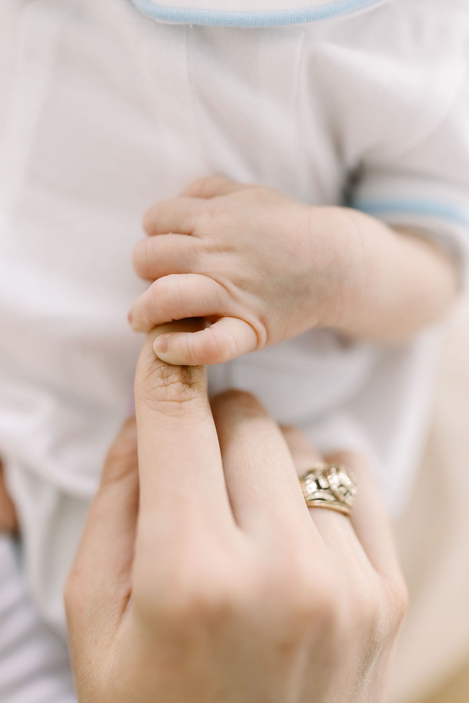 Close up of holding tiny baby hand with engagement ring visible.