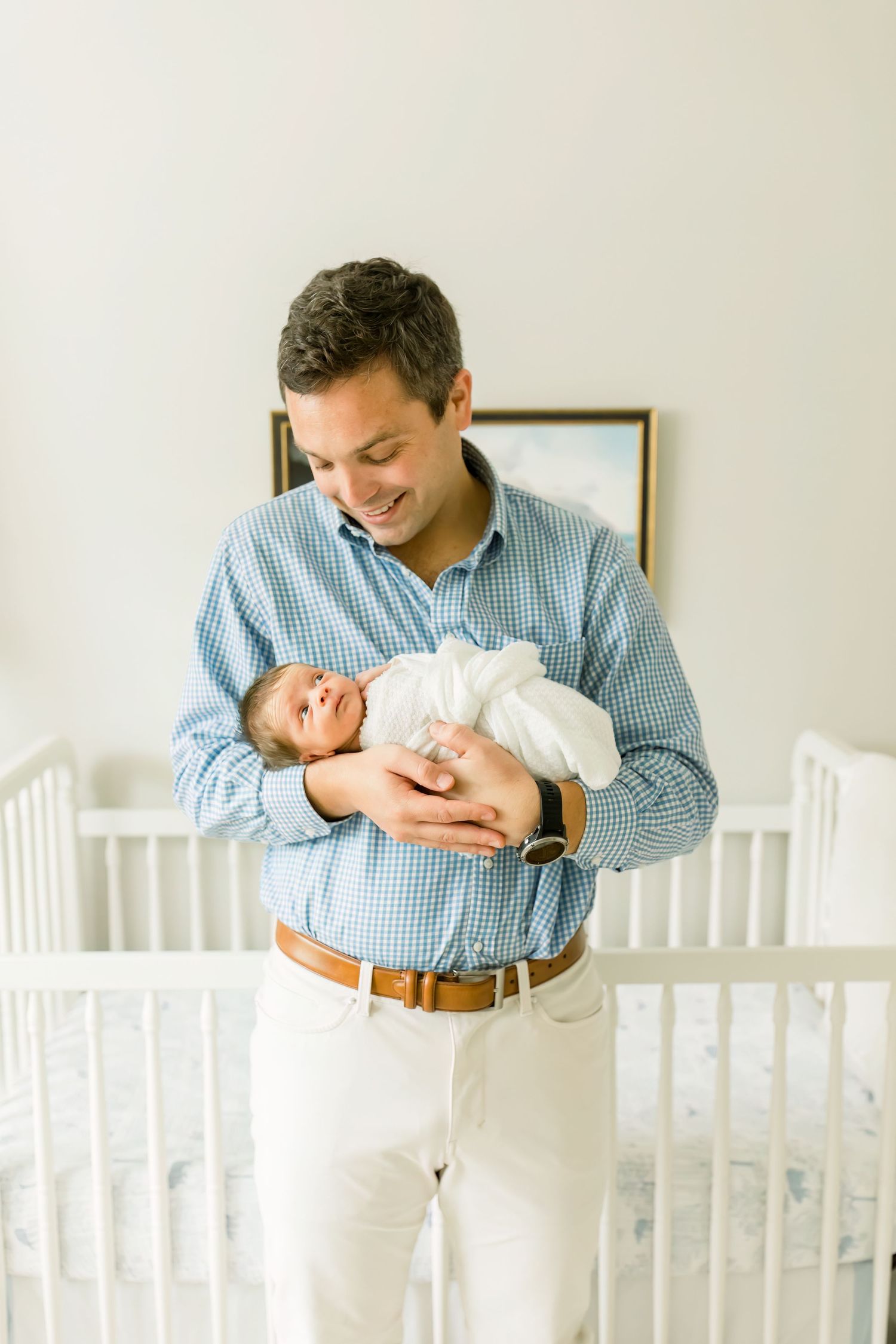 Tender moment between parent and infant in white nursery.