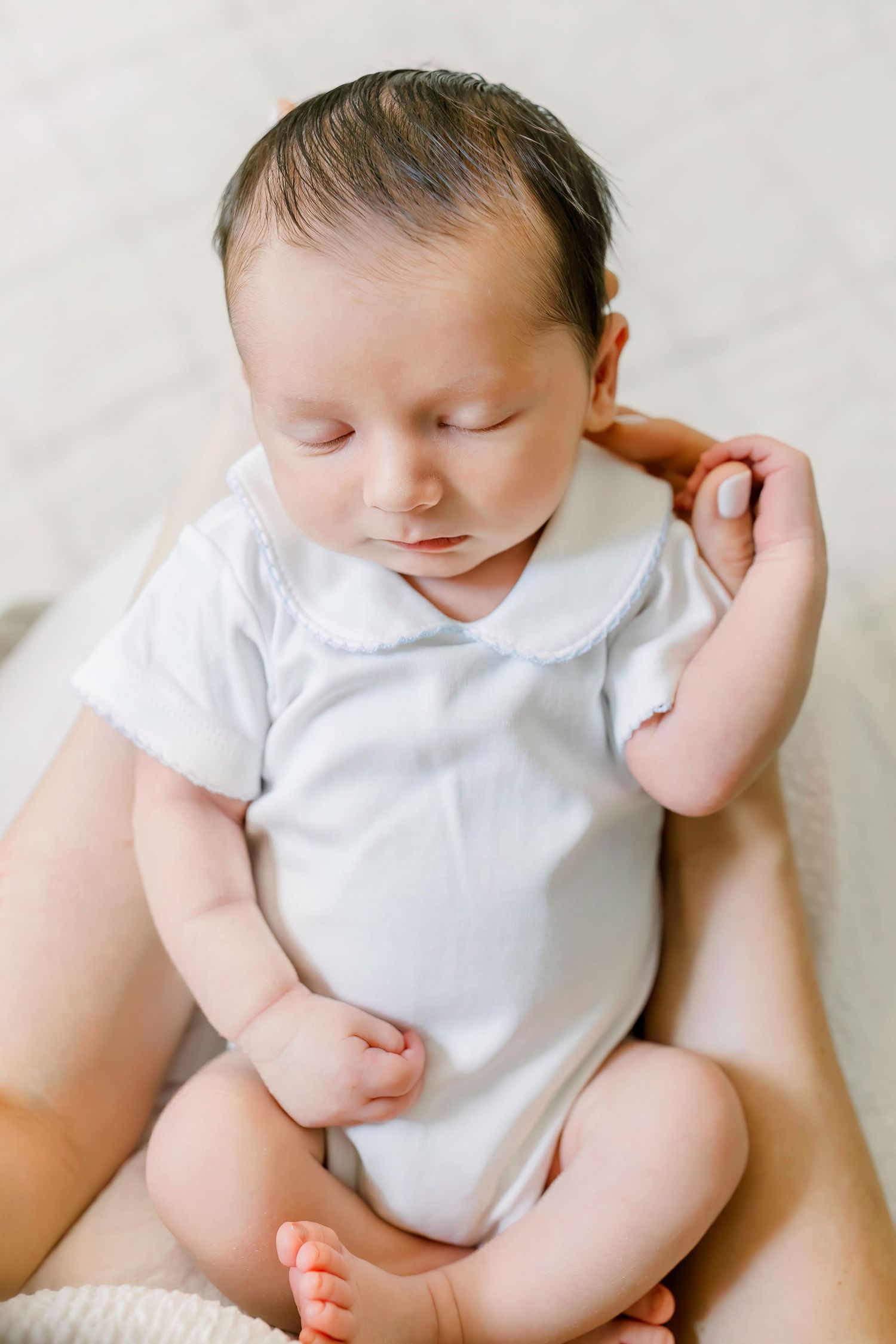Sleeping baby wearing white onesie rests peacefully against soft background.