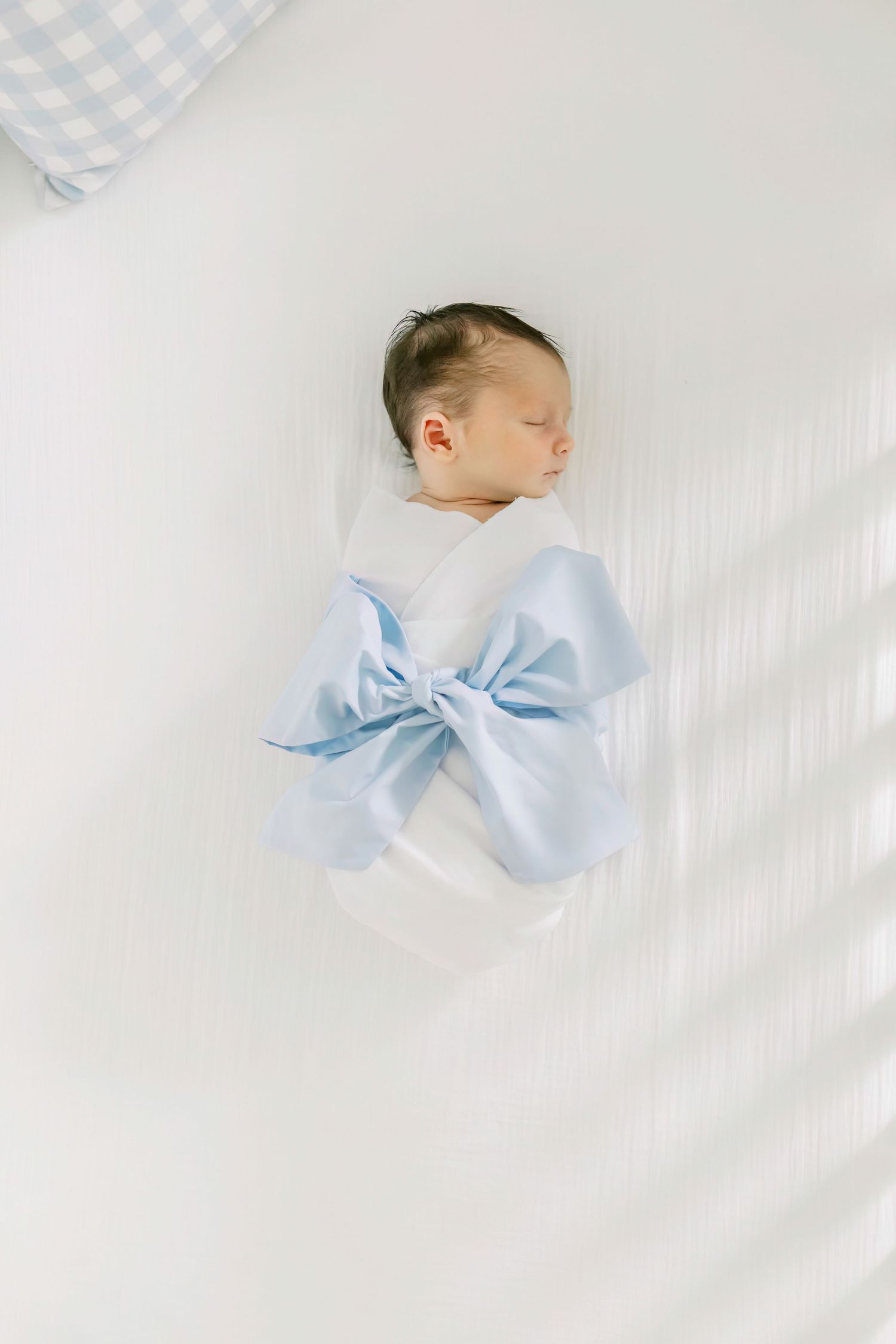 Newborn baby swaddled in light blue wrap with bow on white background.