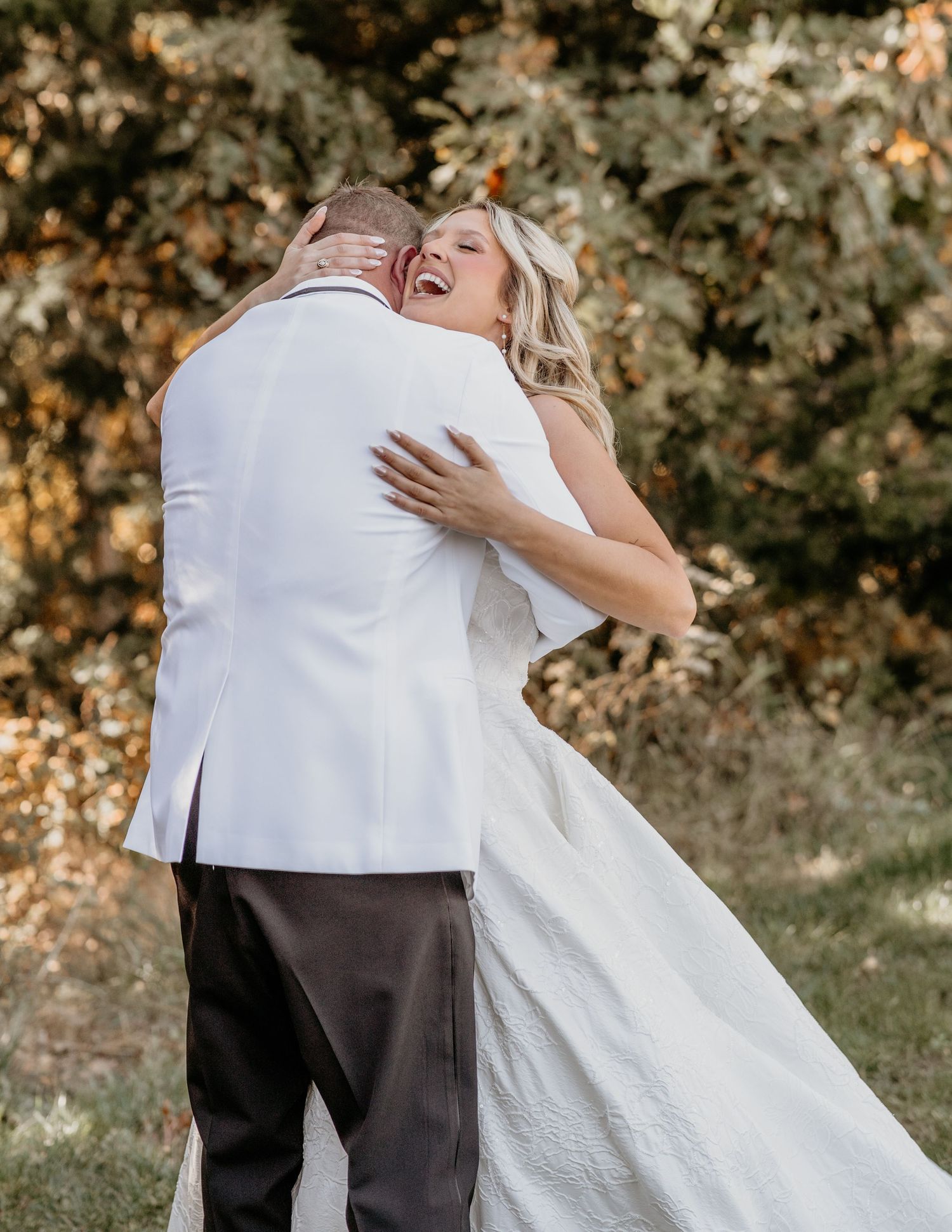A joyful wedding couple embraces and laughs together outdoors during an autumn photo session.