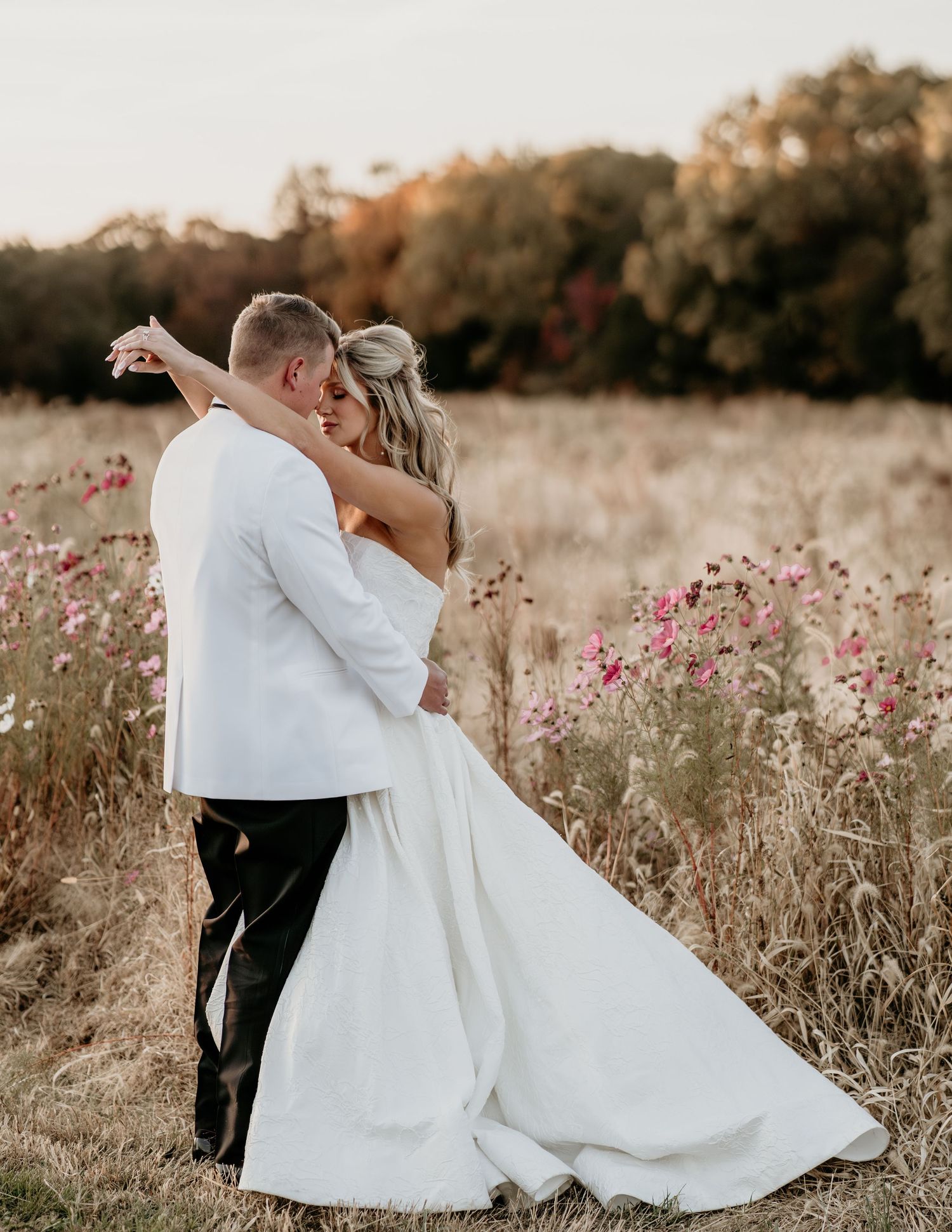 A couple embraces in a romantic autumn field filled with pink wildflowers during sunset.