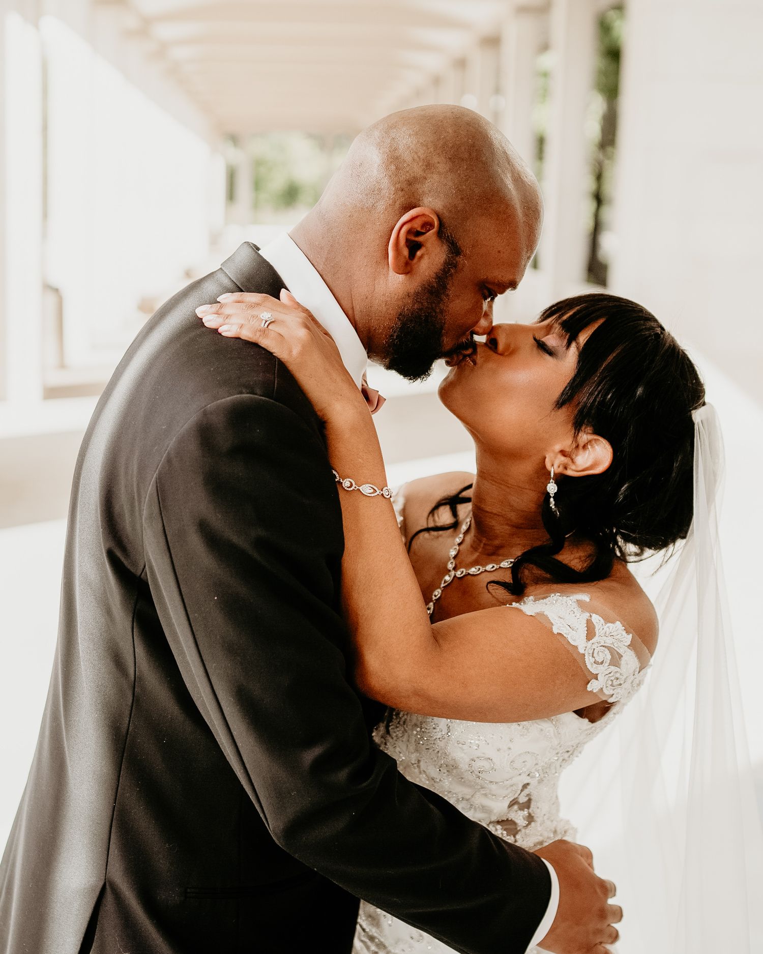A romantic wedding moment of a happy couple sharing a tender kiss in a sunlit venue.