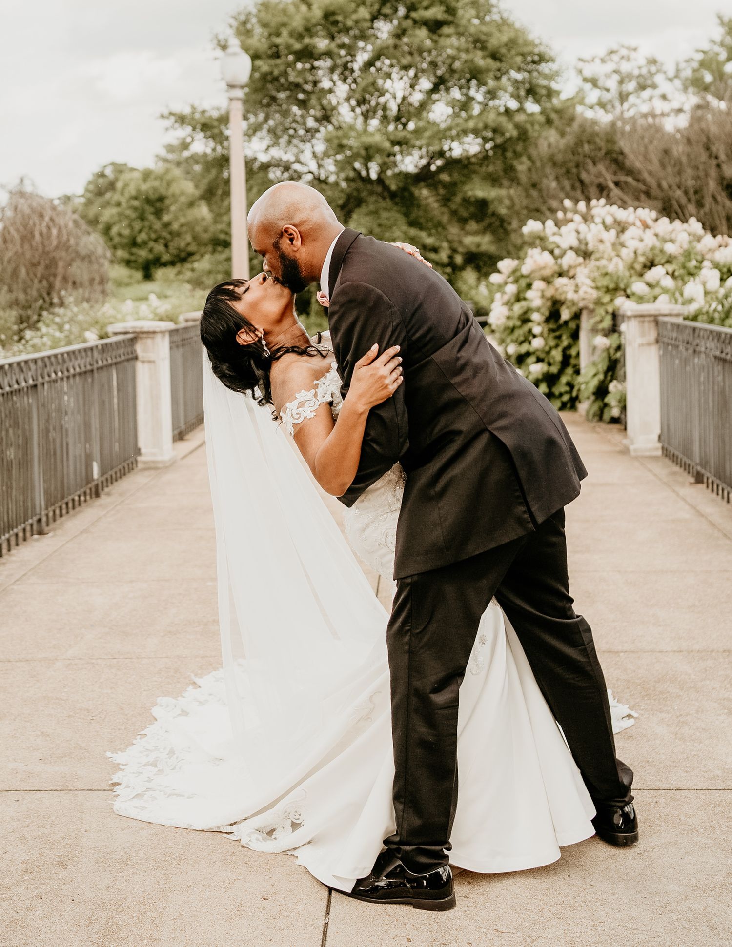 A romantic wedding moment captured on a garden bridge with white floral blooms in the background.