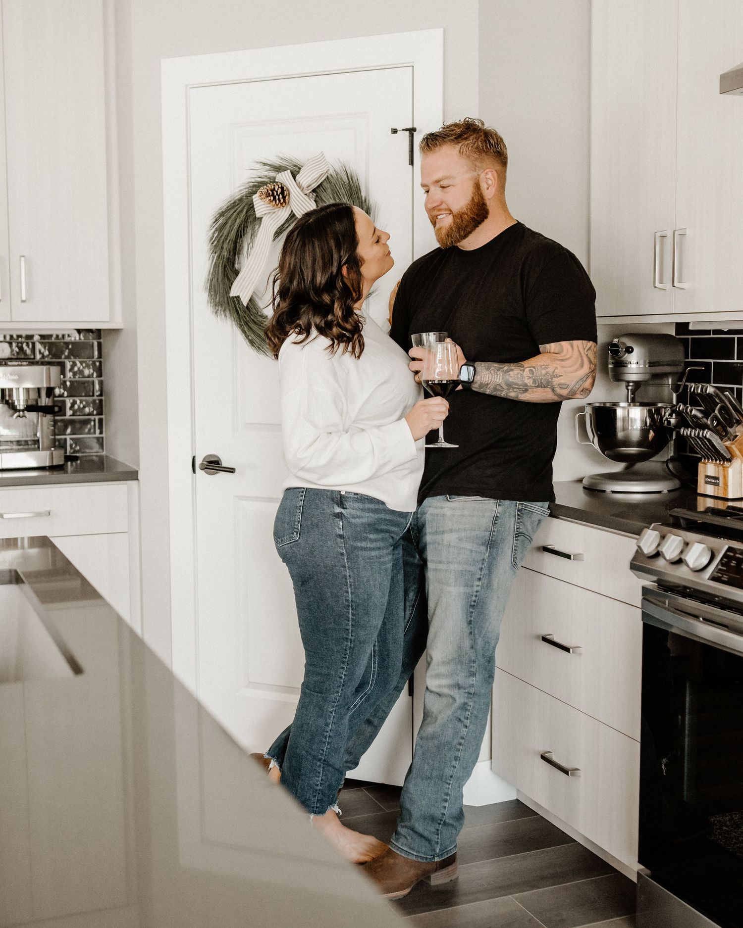 A couple shares an intimate moment together while enjoying wine in their modern white kitchen interior.