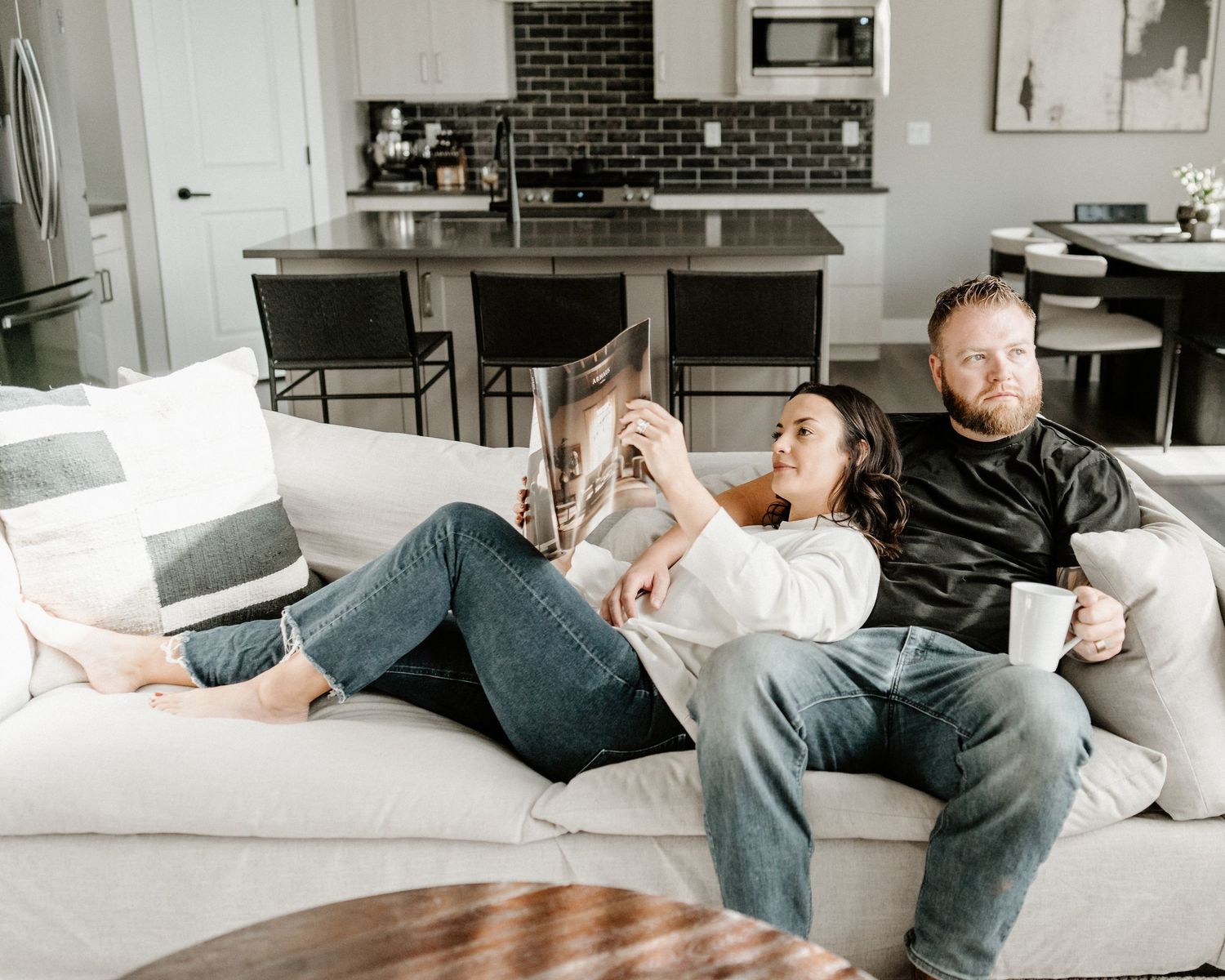 Two people relaxing together on a comfortable white couch in a modern living room with exposed brick wall.