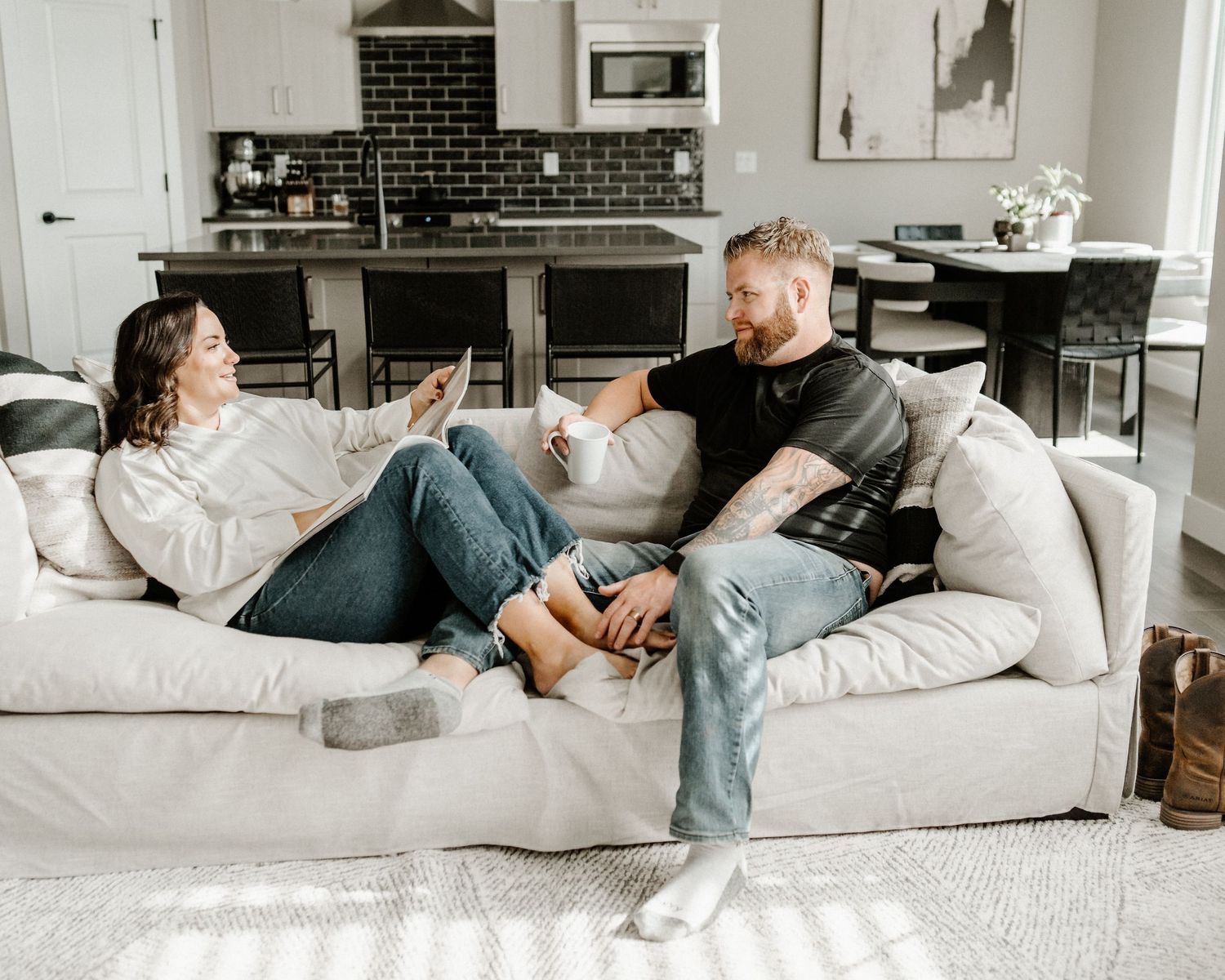 Two people relaxing and talking while lounging on a comfortable white couch in a modern living room.