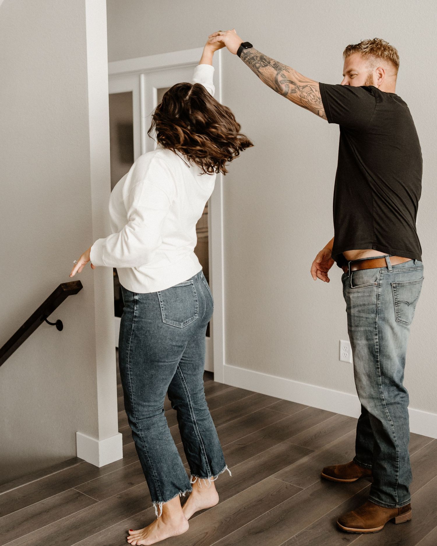 Two people dancing together on hardwood floors beside white walls in a casual indoor setting.