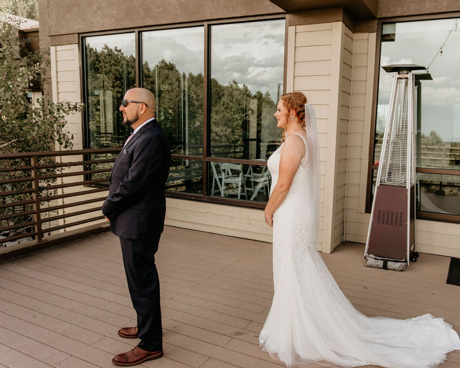 Two people share a first look moment on a modern apartment balcony with glass panels and scenic views.