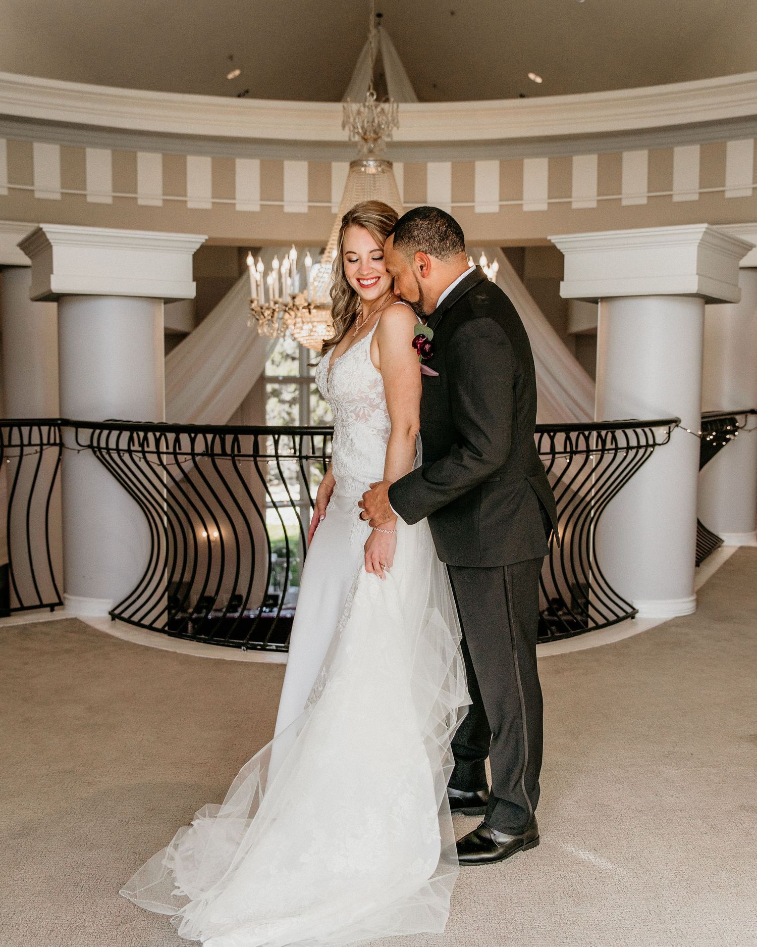 A couple shares a joyful moment in an elegant venue with white columns and a crystal chandelier.