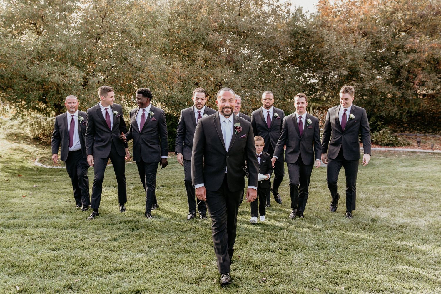 Group in formal attire walking across a grassy lawn during a wedding celebration in autumn.