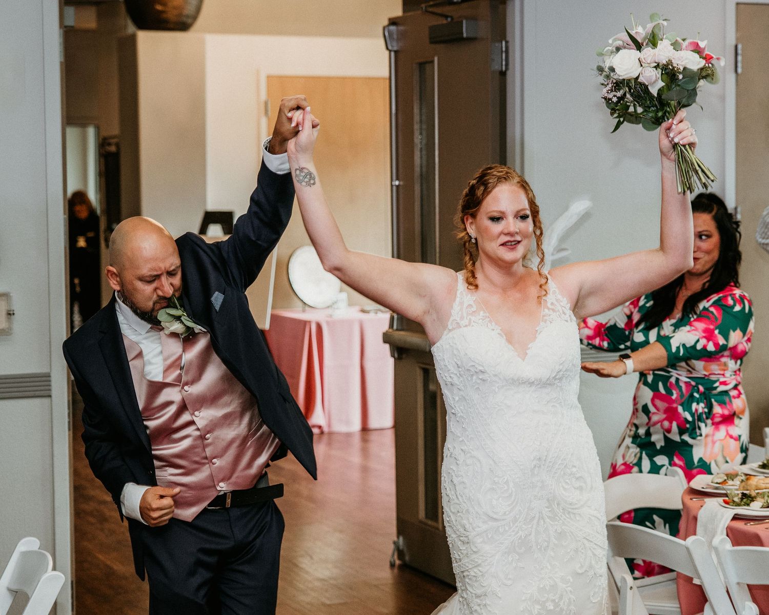 A couple makes their grand entrance at a wedding reception with raised arms and celebratory gestures.