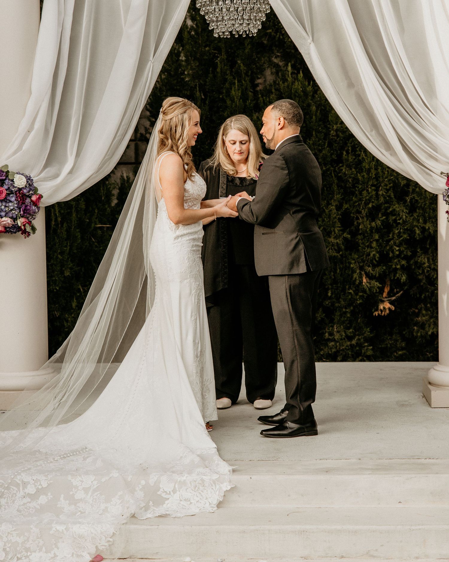 Wedding ceremony takes place under an elegant draped white canopy with an officiant and couple during the vows.