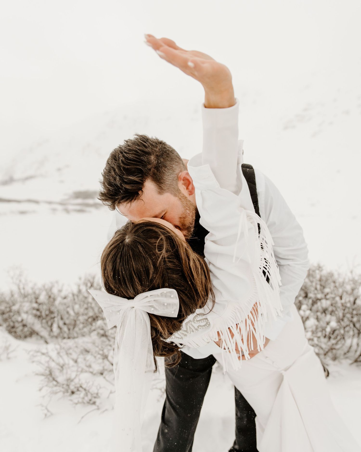 A couple dancing together in winter snow wearing white and black outfits against a serene snowy landscape.