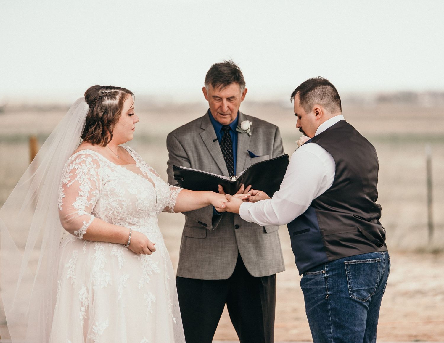 A couple shares their wedding ceremony outdoors with an officiant reading from a book during a desert ceremony.