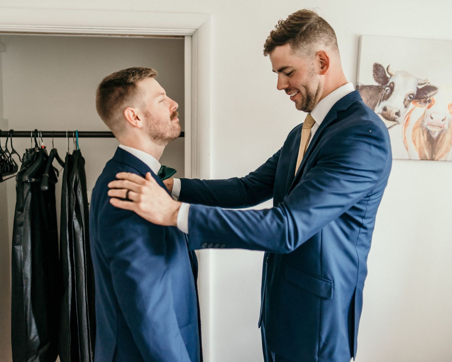 Two people in matching navy suits sharing a joyful moment in a dressing room.