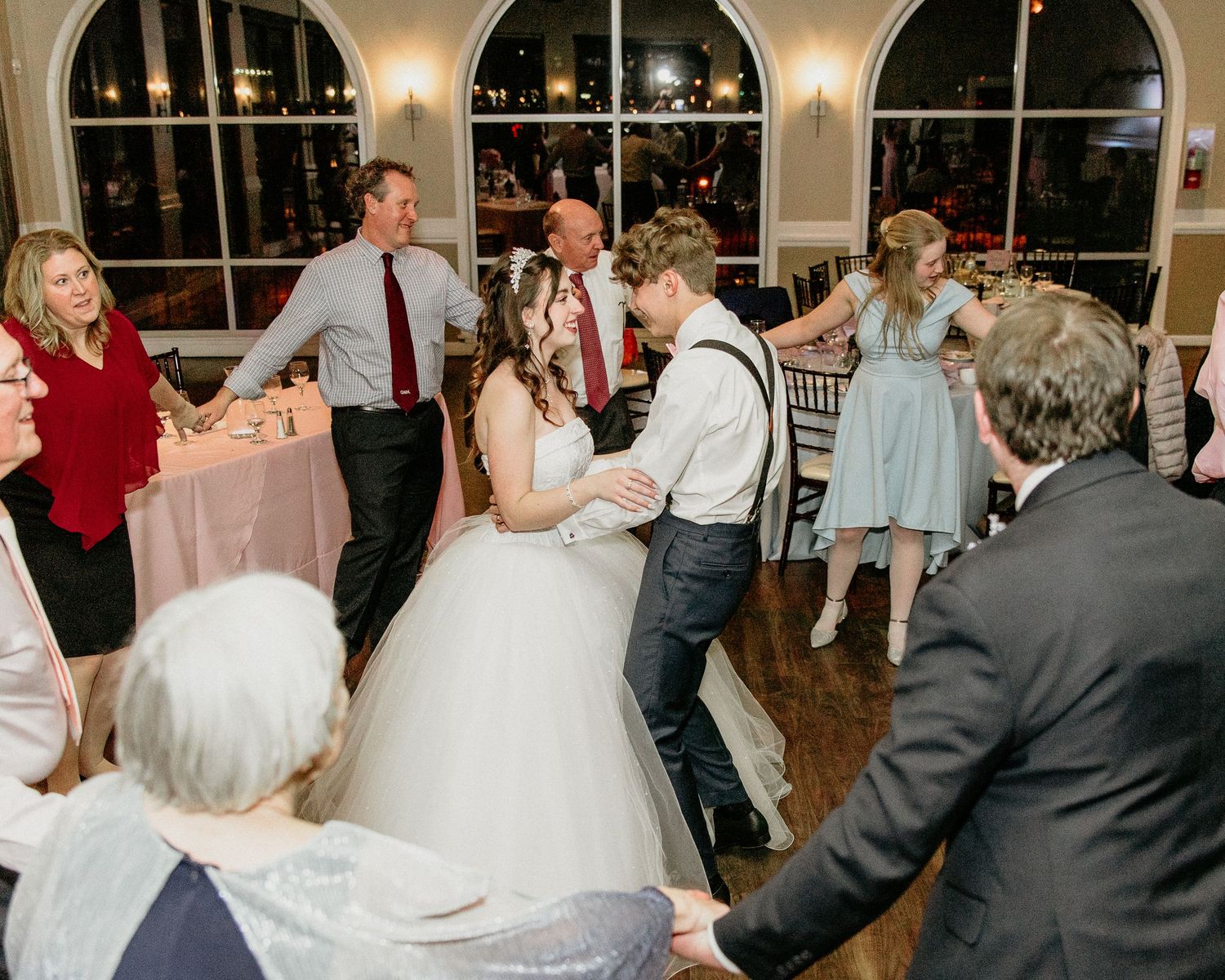 Wedding guests dance together on a ballroom floor during an evening reception celebration.