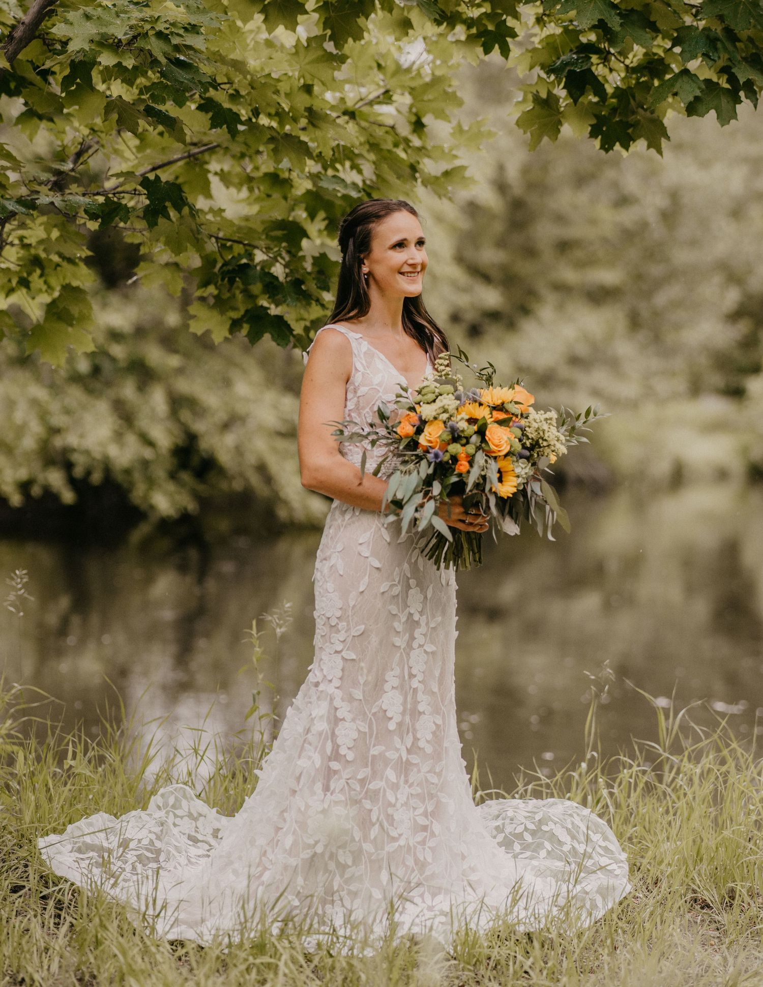 Lace wedding dress and sunflower bouquet photographed in a dreamy outdoor garden setting.
