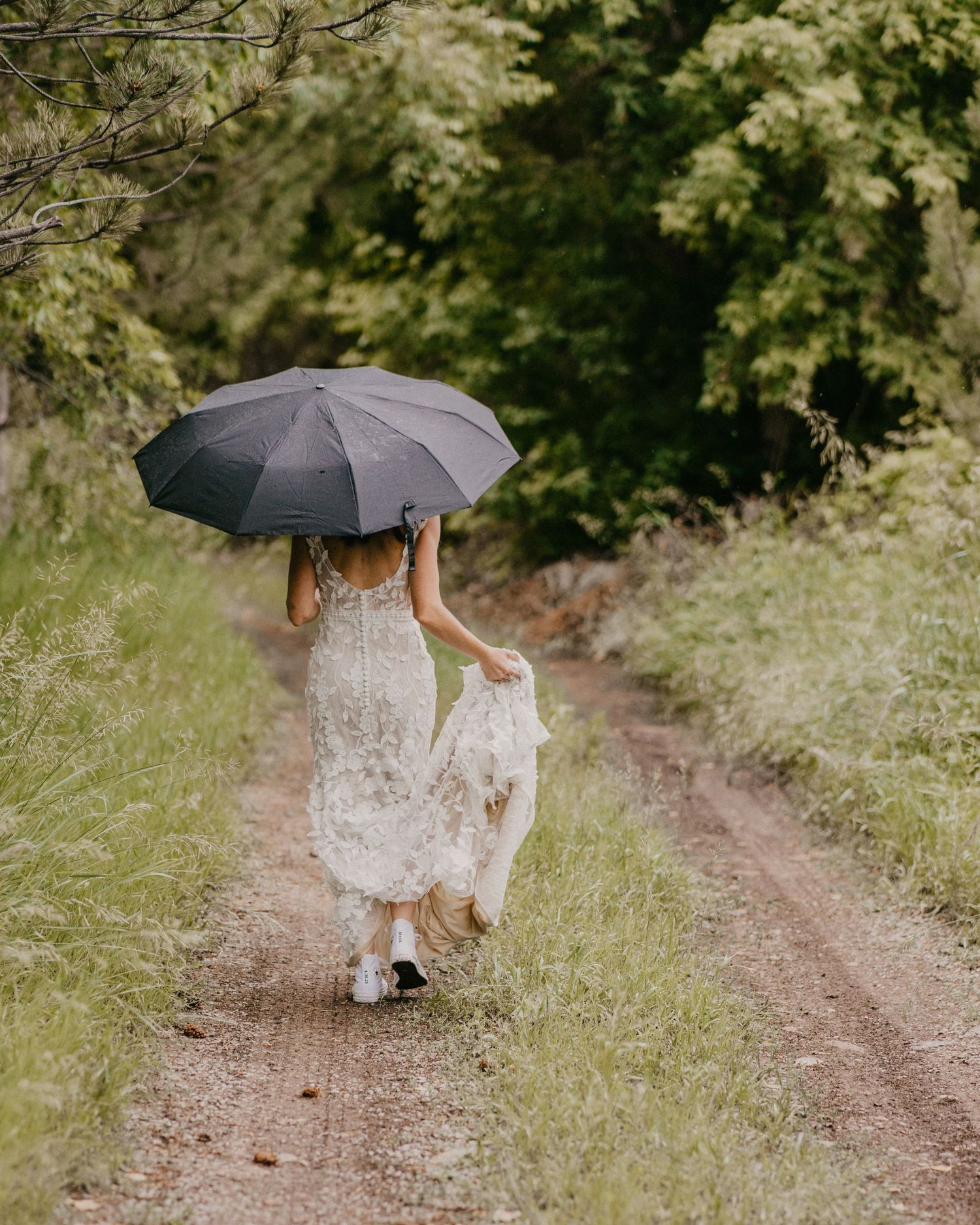 Ethereal wedding photo of dress trailing on dirt path while holding black umbrella.