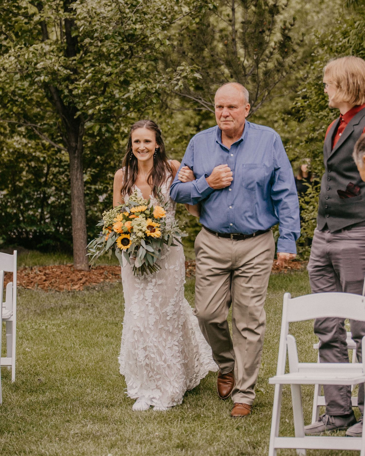 Walking down the aisle after an outdoor wedding ceremony with sunflowers in the bouquet.