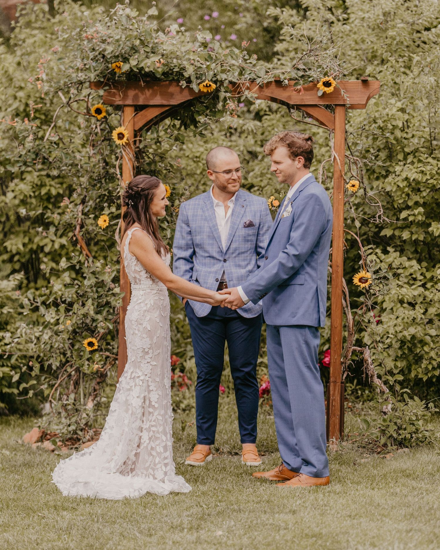 Wedding ceremony under a rustic wooden arch decorated with sunflowers and greenery.