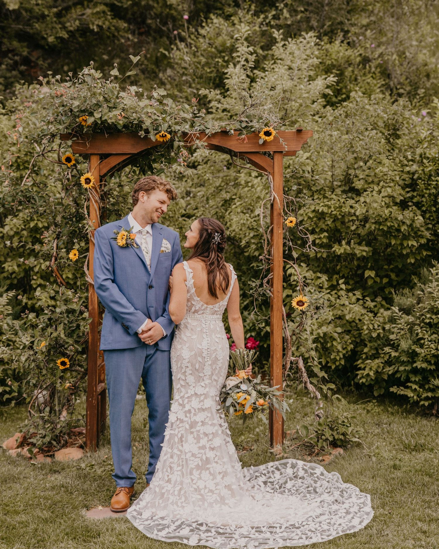 Romantic outdoor wedding ceremony under wooden arch decorated with florals and greenery.