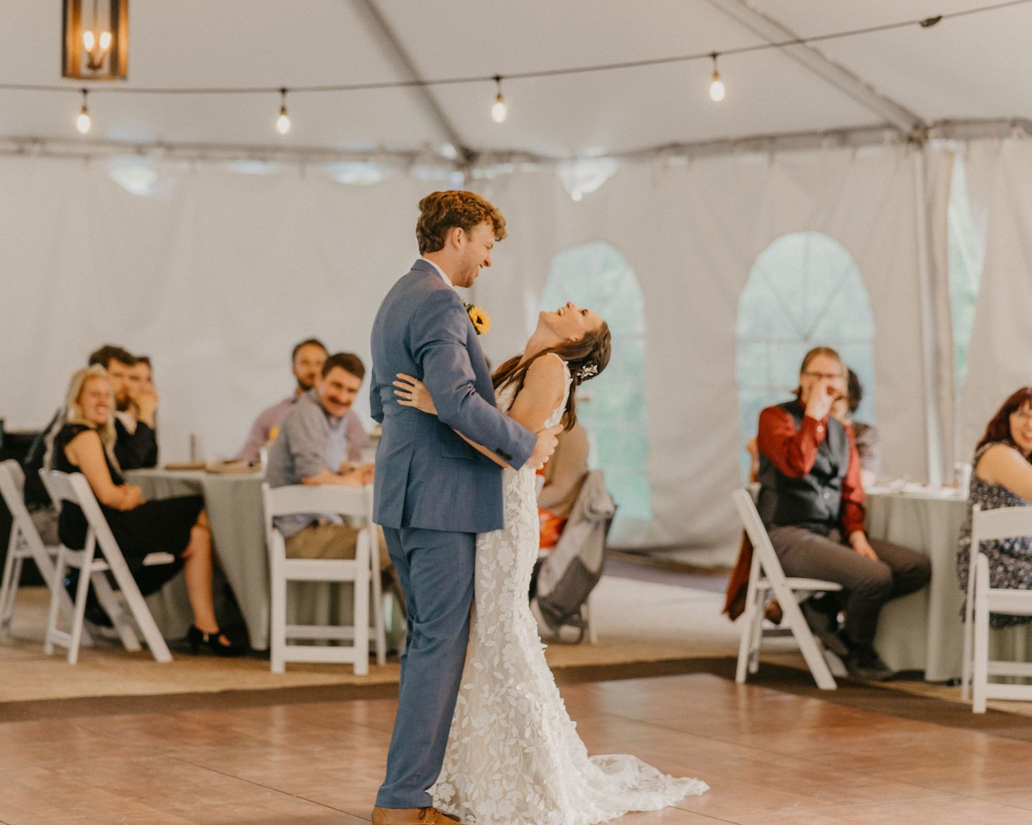 Wedding couple shares a romantic dance moment under string lights at their reception.