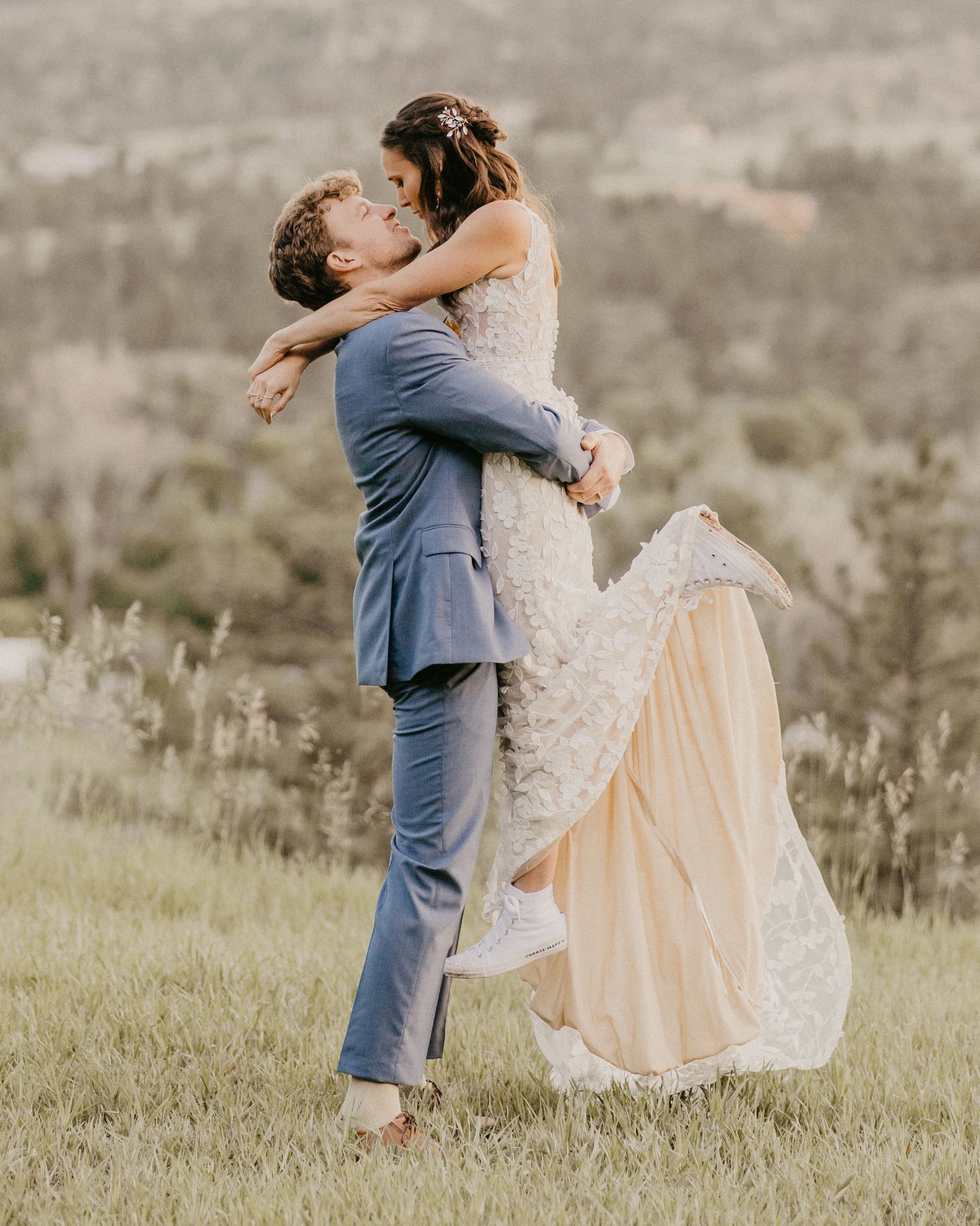 A romantic wedding moment captured as the couple embraces in a scenic meadow with mountain backdrop.