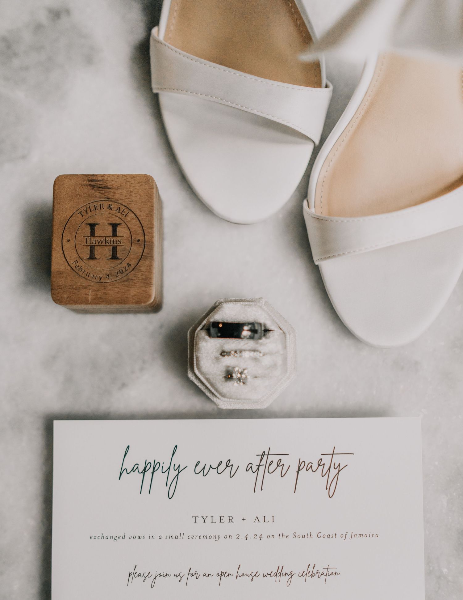 Wedding details flat lay with white shoes, wooden box, ring box and invitation card.