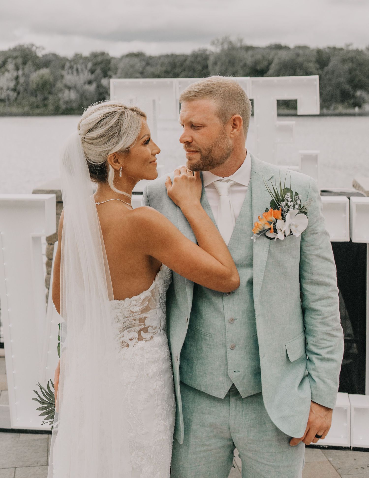 Intimate wedding portrait on lakeside terrace with mint green suit and lace gown.