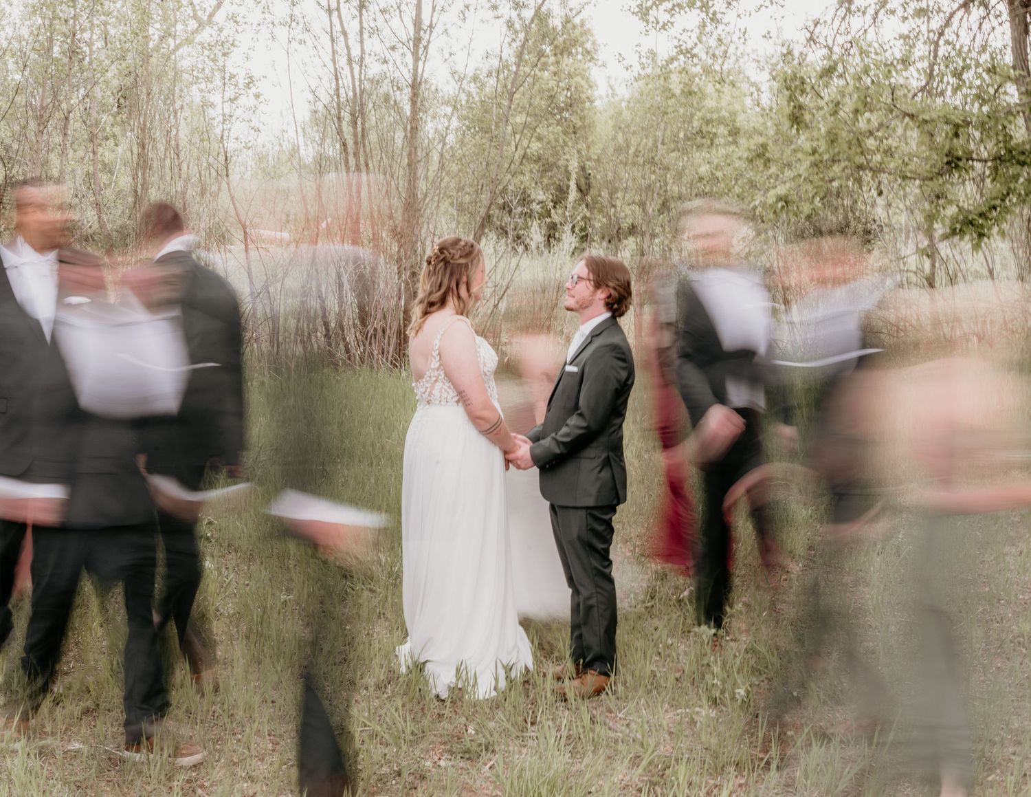 Motion blur surrounds newlyweds during outdoor wedding ceremony in a natural wooded setting at dusk.