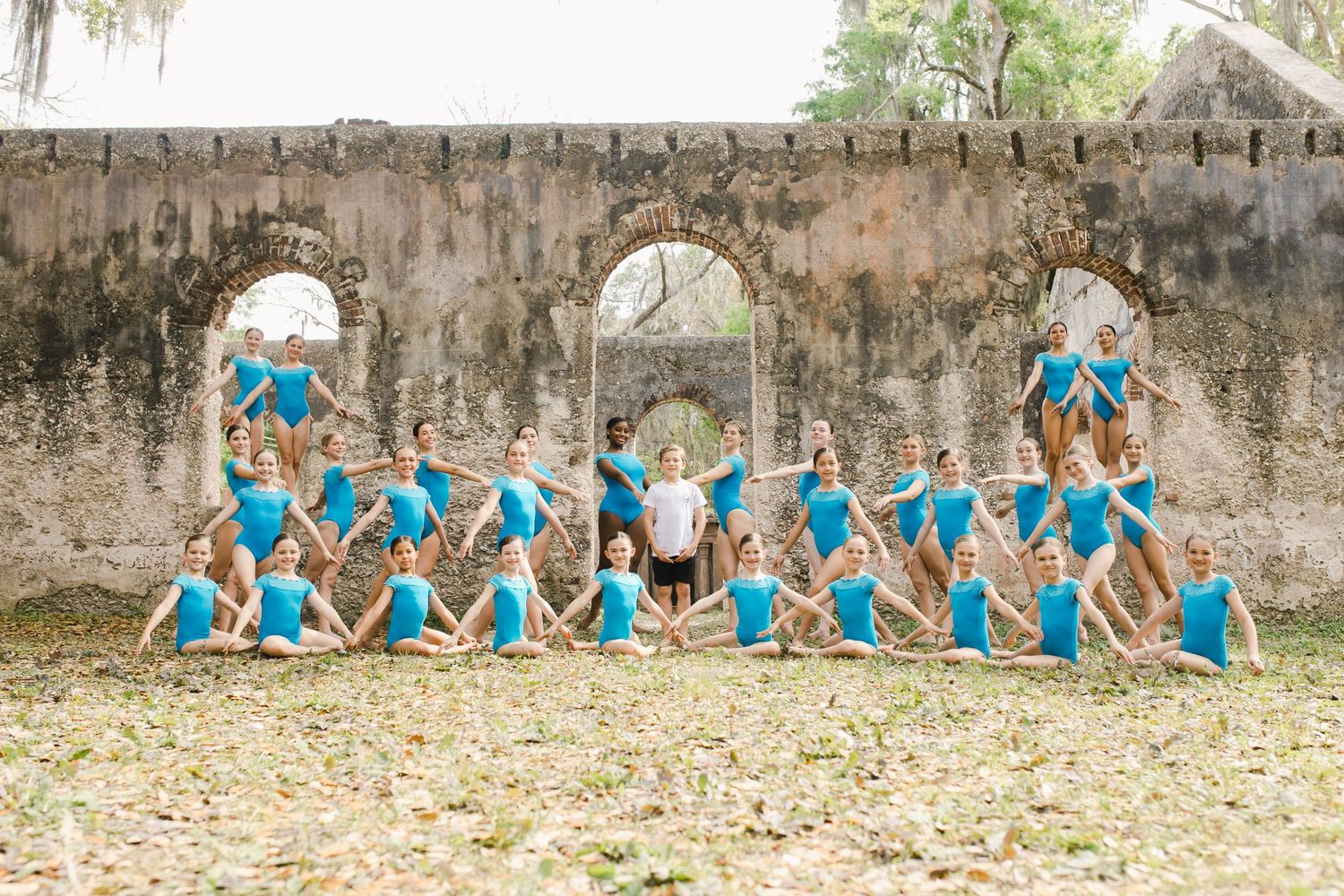 Group of dancers in blue leotards posing for photographer in formation outdoors near historic stone ruins in Saint Helena, South Carolina.